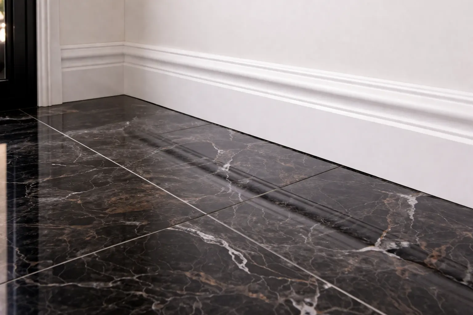 Close-up of hand-wiped white baseboards and polished black marble floors after a professional deep clean.