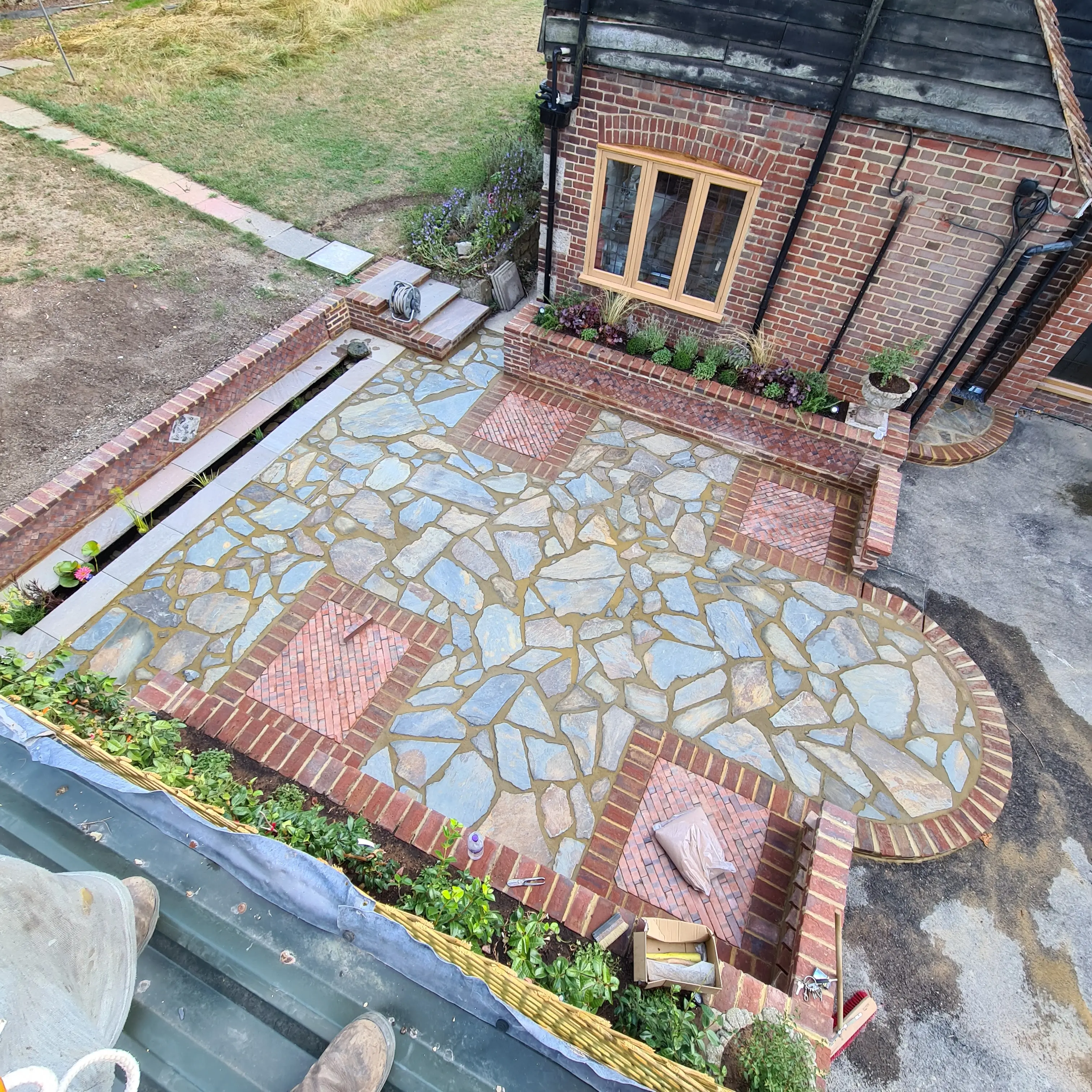 Aerial view of a stone patio, featuring intricate patterns and a landscaped border with a house nearby.