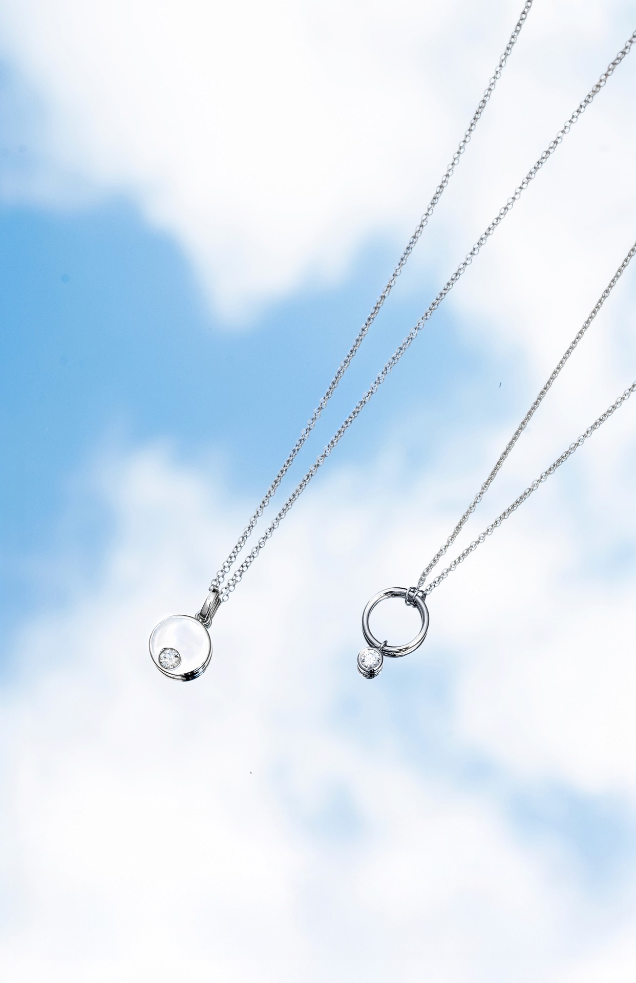 product photography of two silver necklaces laying on a mirror under a sunny sky filled with clouds.