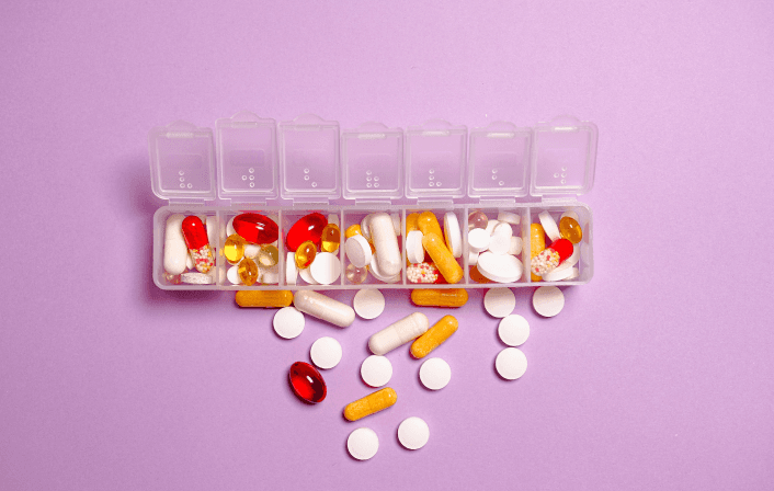 Weekly pill organizer with assorted medications spilled out.