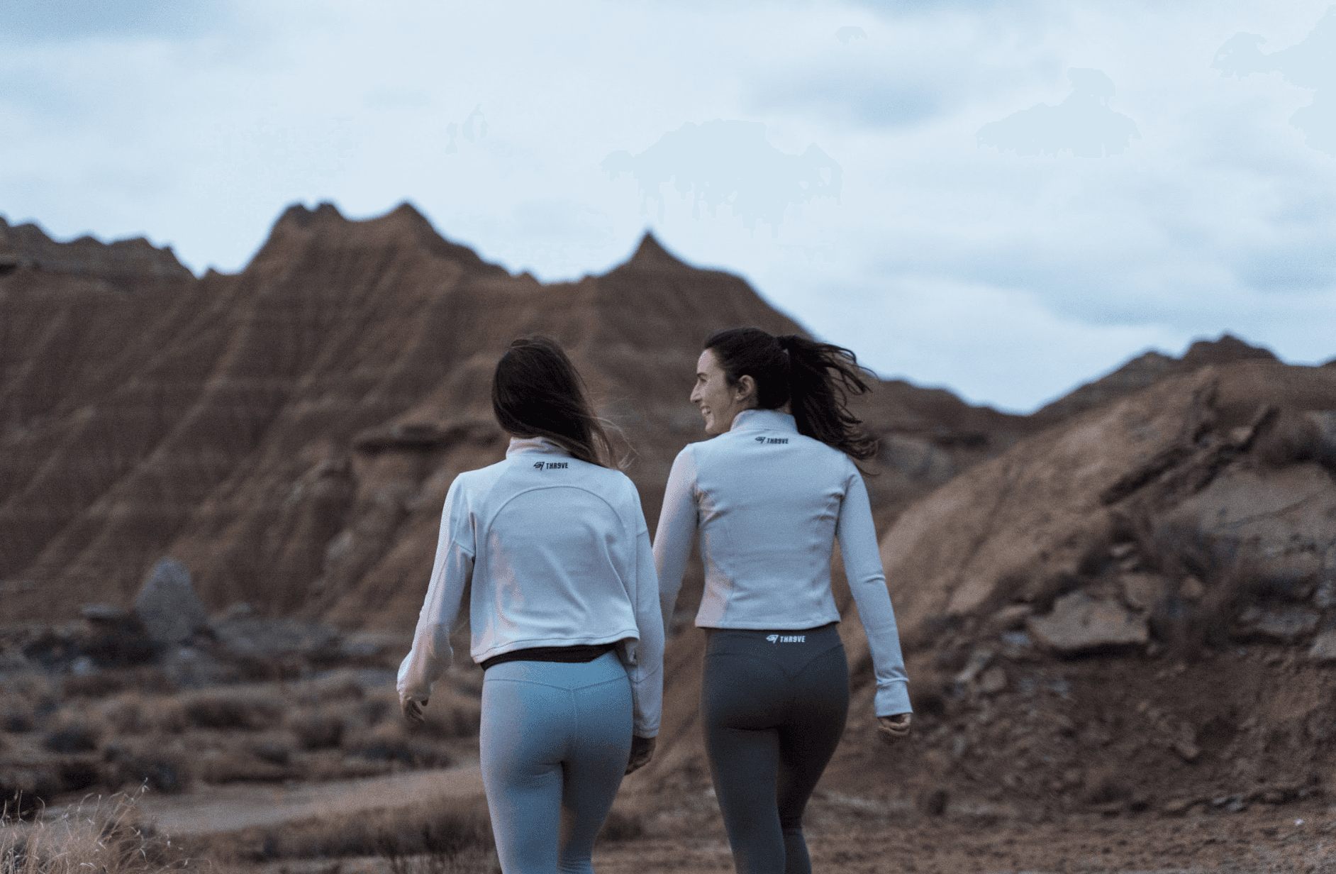 Man wearing olive green and orange sneakers with tall socks, standing on an urban street with a modern fence and skyscraper in the distance.