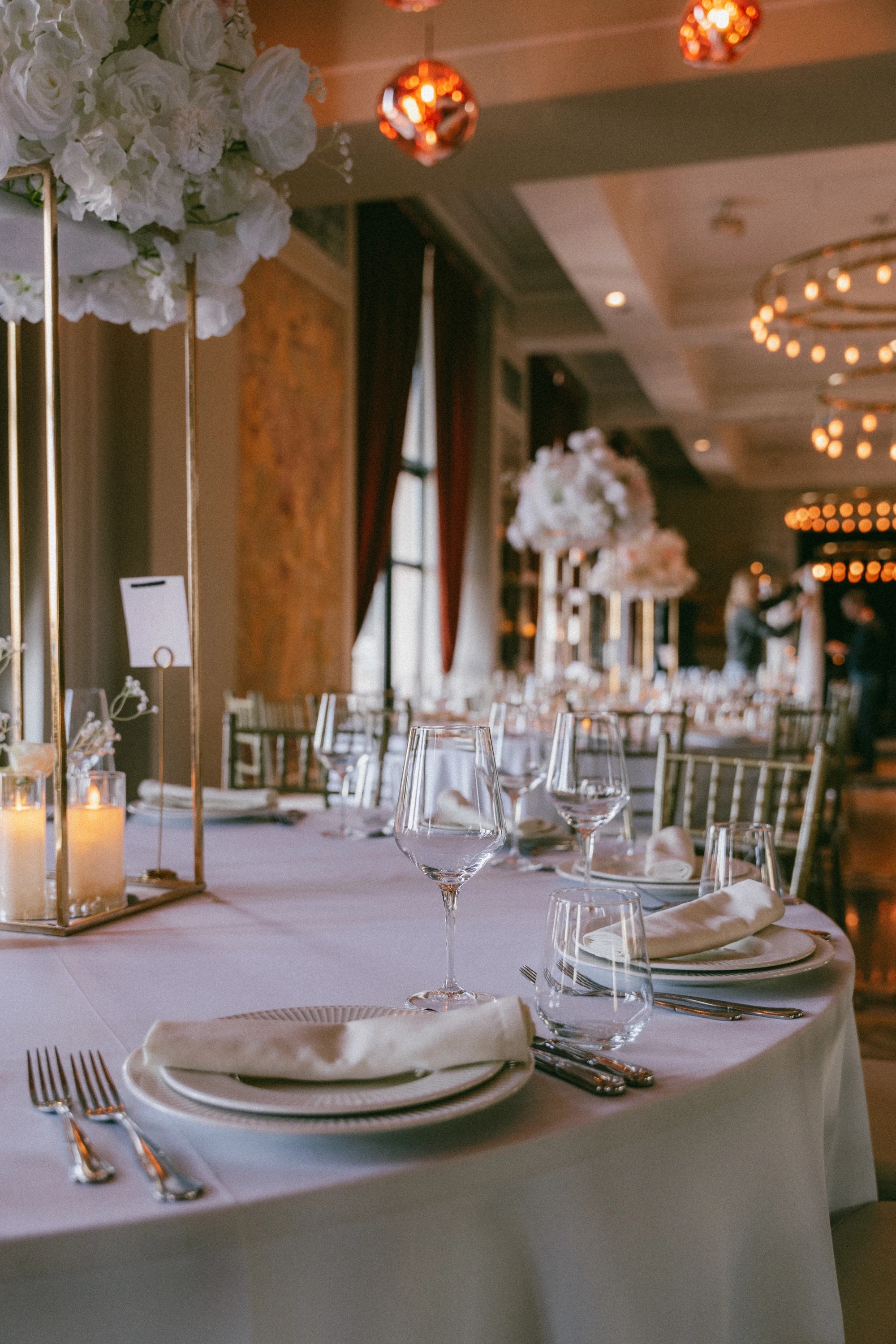 ქორწილის სუფრის გაფორმება თეთრი სუფრით, ბროლის ჭიქებით, სანთლებითა და ვარდისფერი ყვავილების დეკორით