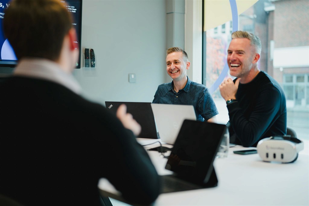 Two men discuss a project while standing at a laptop in an office.
