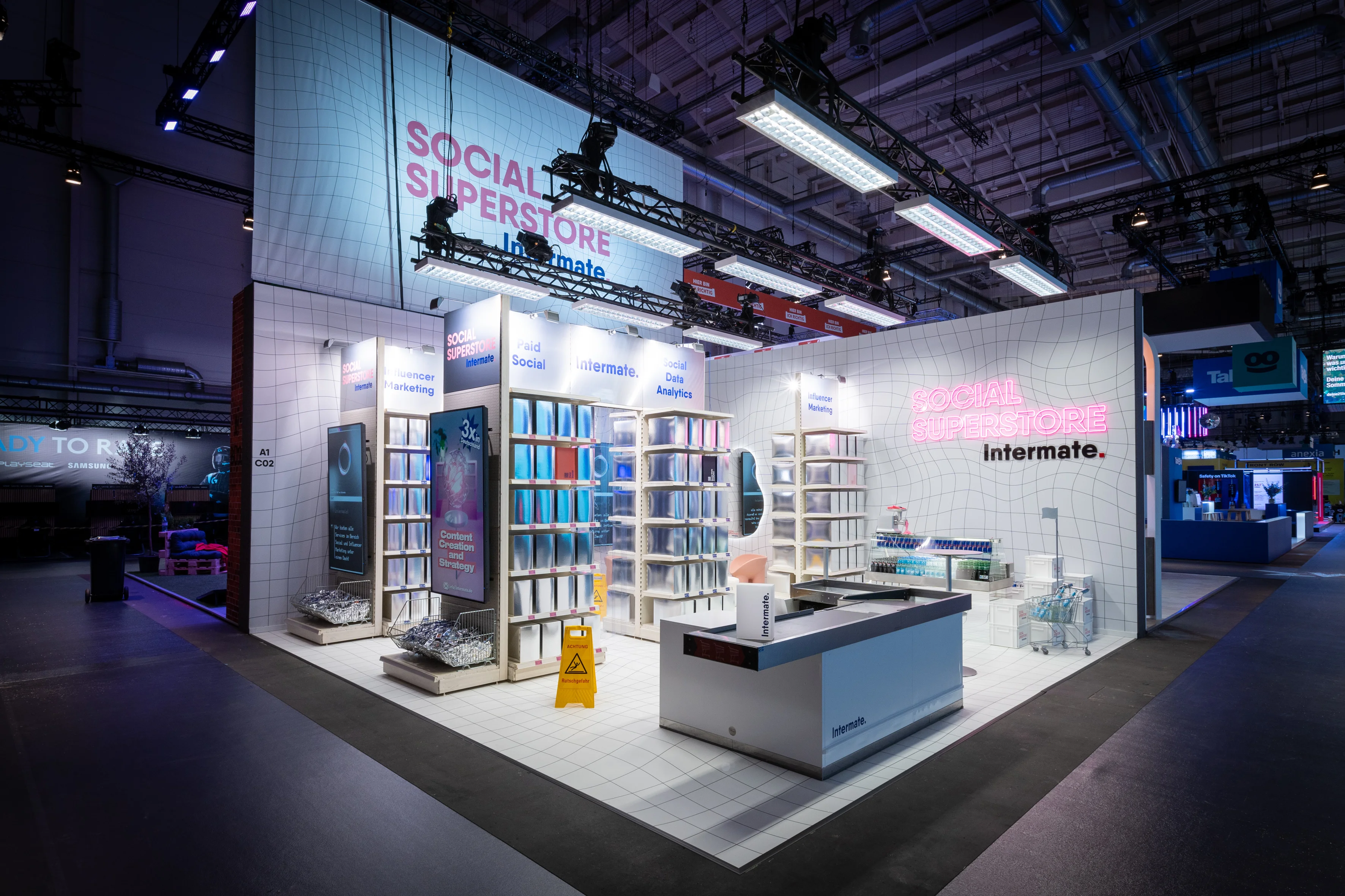 The Intermate Social Superstore booth at OMR with white grid architecture, illuminated banner and pink neon lettering.