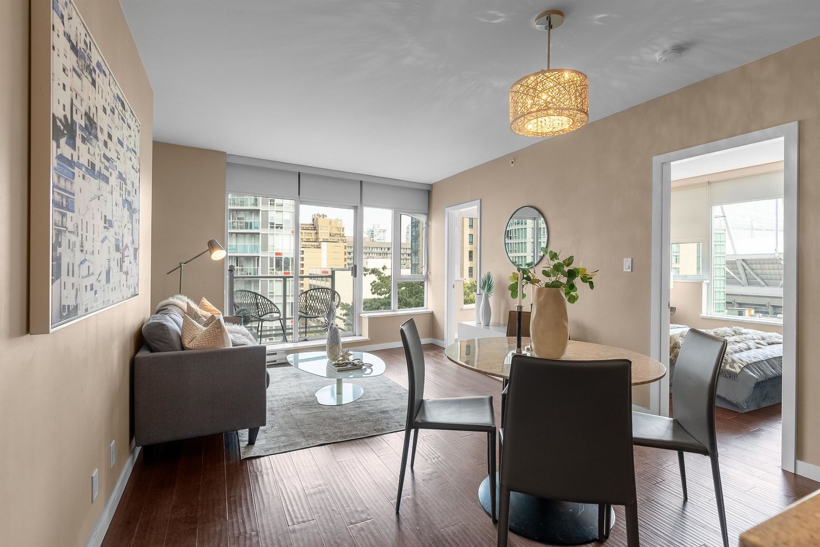 A cozy living room with large windows, light walls, and potted plants, featuring comfortable seating and warm lighting.