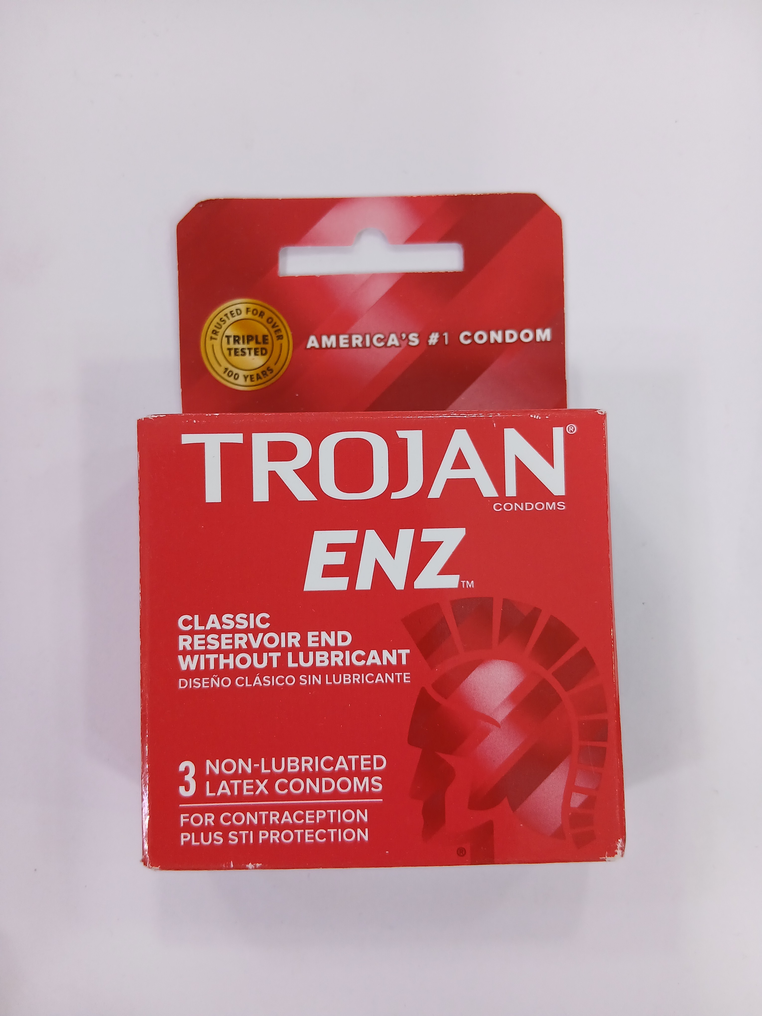 A red cardboard box packaging displays three non-lubricated latex condoms in a blister pack, featuring text in English and Spanish and a gold seal at the top.