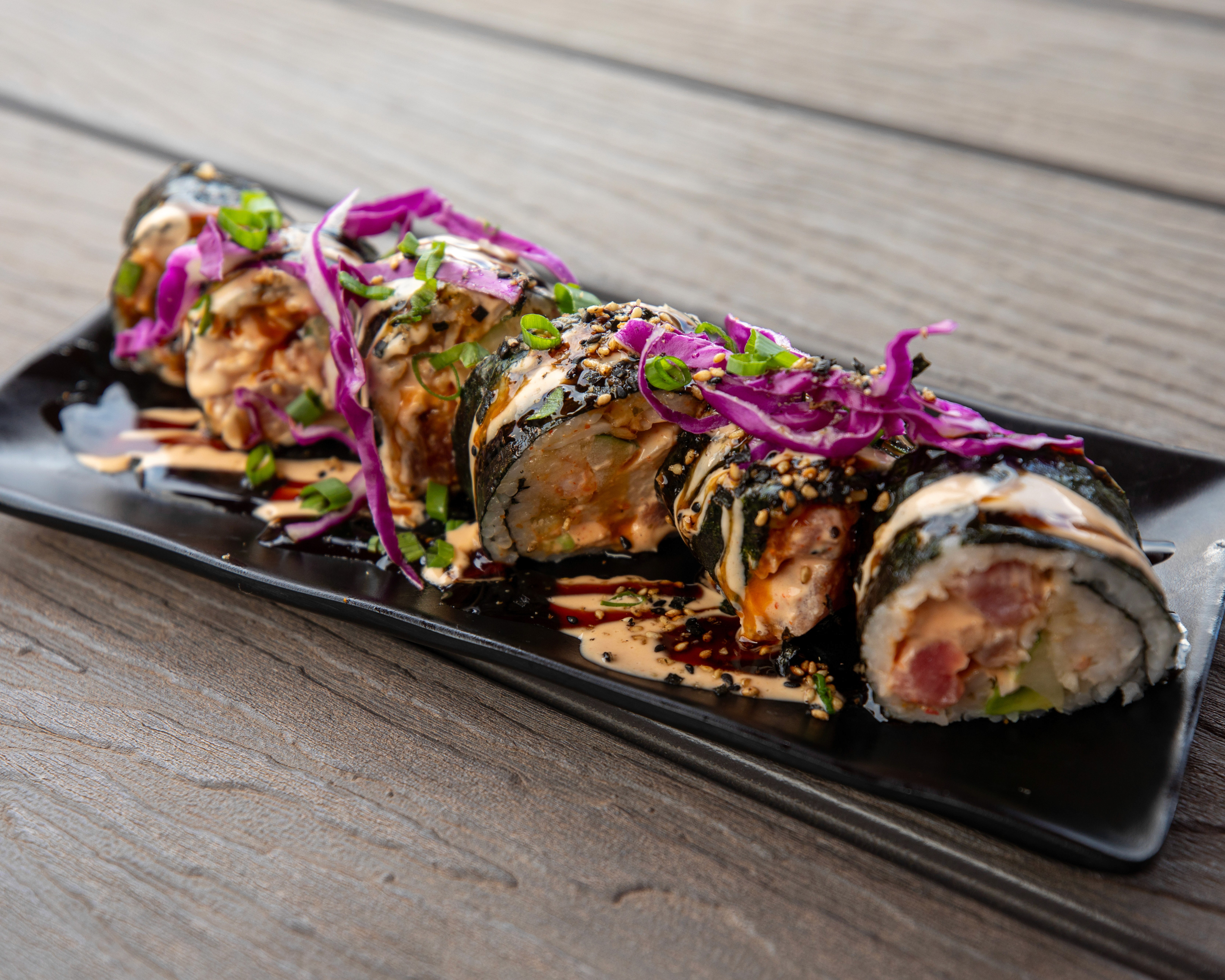 An overhead shot of a plate of spaghetti tossed with creamy sauce, large leaves of spinach, and dark beans or olives, garnished with shredded cheese and served on a wooden board.