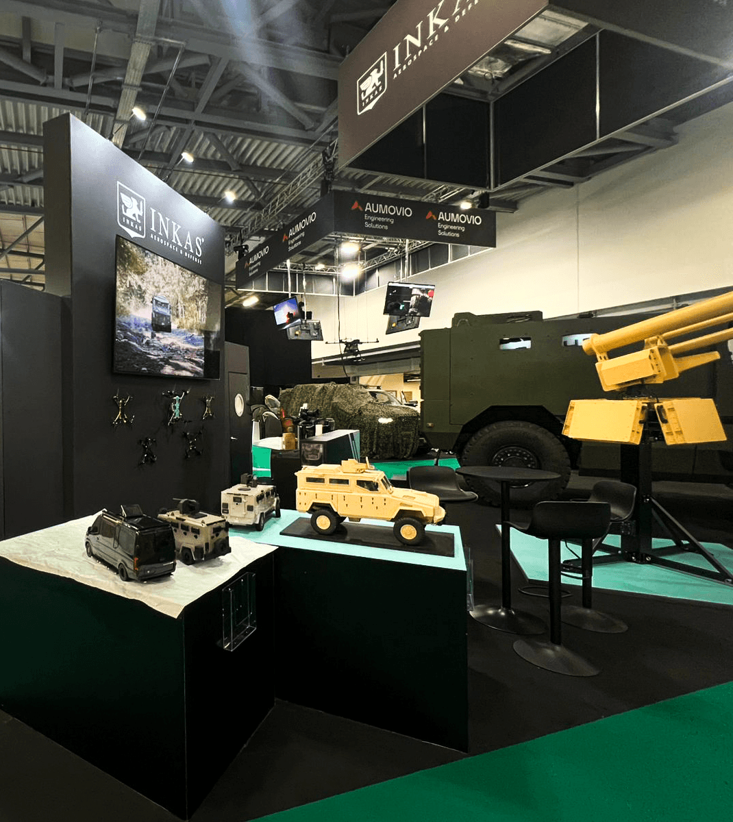 Stand INKAS Armored Farnborough 2026 réalisé par Expace – vue frontale avec véhicule blindé militaire exposé grandeur nature sur stand vert kaki et noir mat