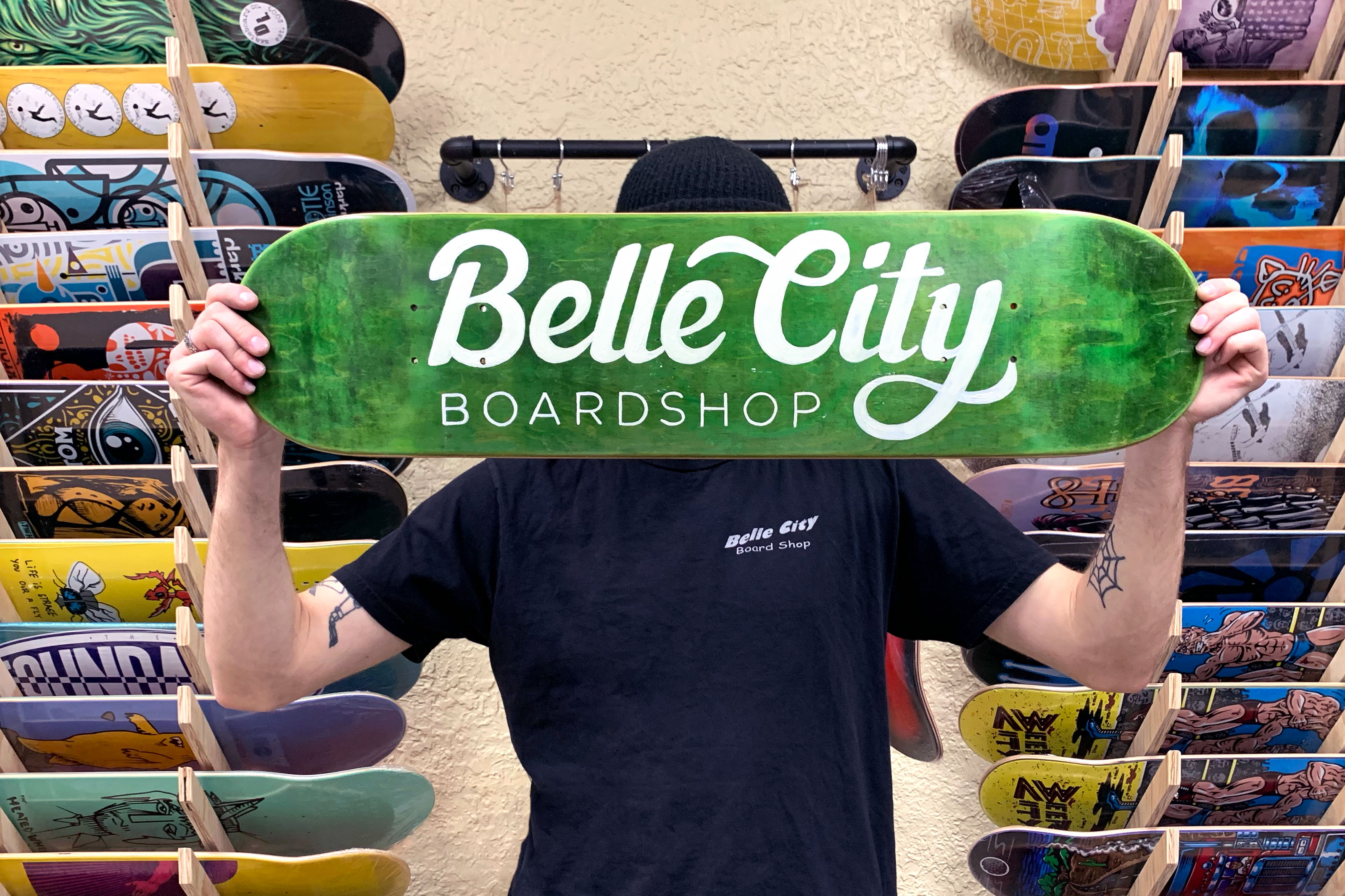 Man holding painted skateboard in skateshop reading Belle City Boardshop