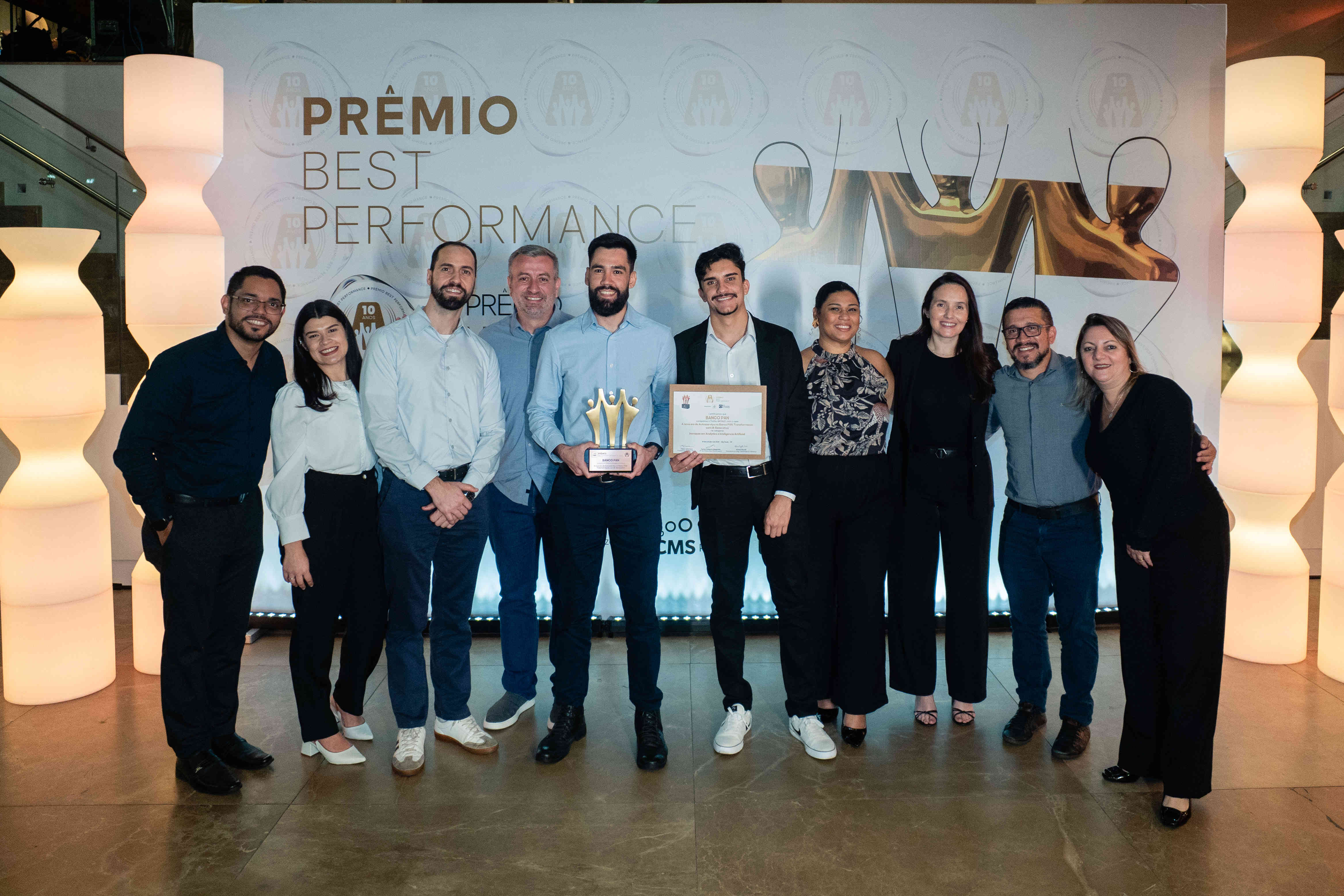 Executivos do BANCO PAN posando com troféu bronze e certificado no palco do Prêmio Best Performance 2025.