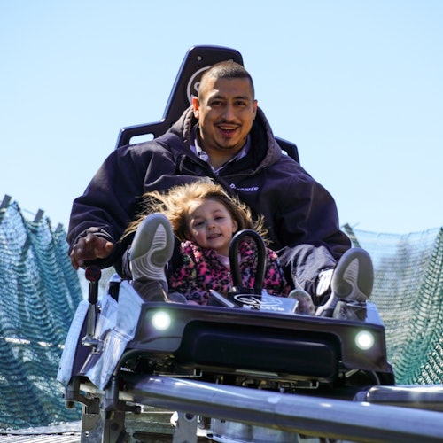 એક સંપૂર્ણ અને બાળક રોલર કોસ્ટર પર ચાલી રહ્યા છે અને હસતા જોવા મળે છે; બાળક પરિપત્ર ચેતાવણીમાં છે, અને તેઓને એક જાળીદાર બારીએ ઘેરવામાં આવ્યું છે.