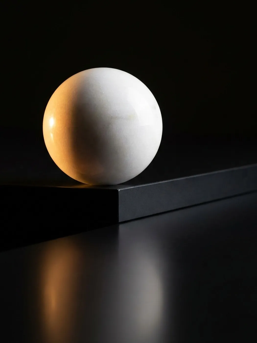 Smooth white sphere on black surface with reflection