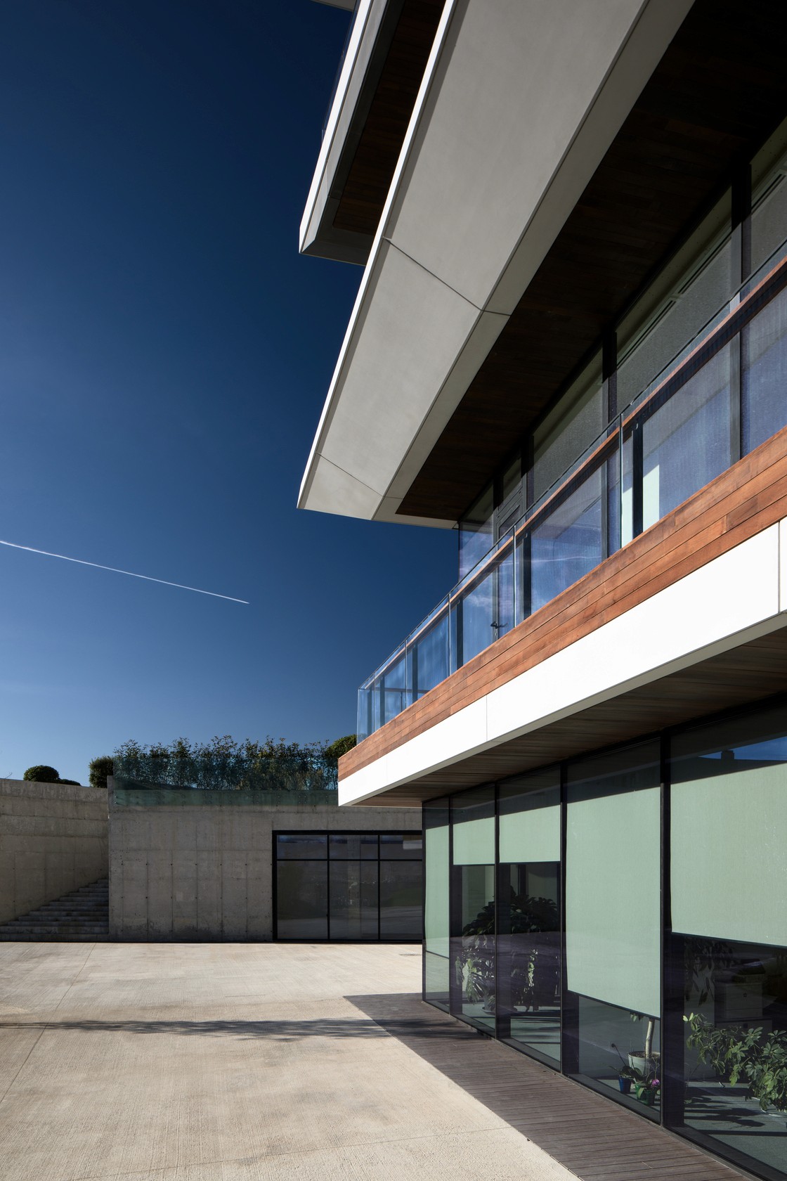 Modern building with a sleek design, large windows, and a terrace under a clear blue sky. Sunny outdoor area.