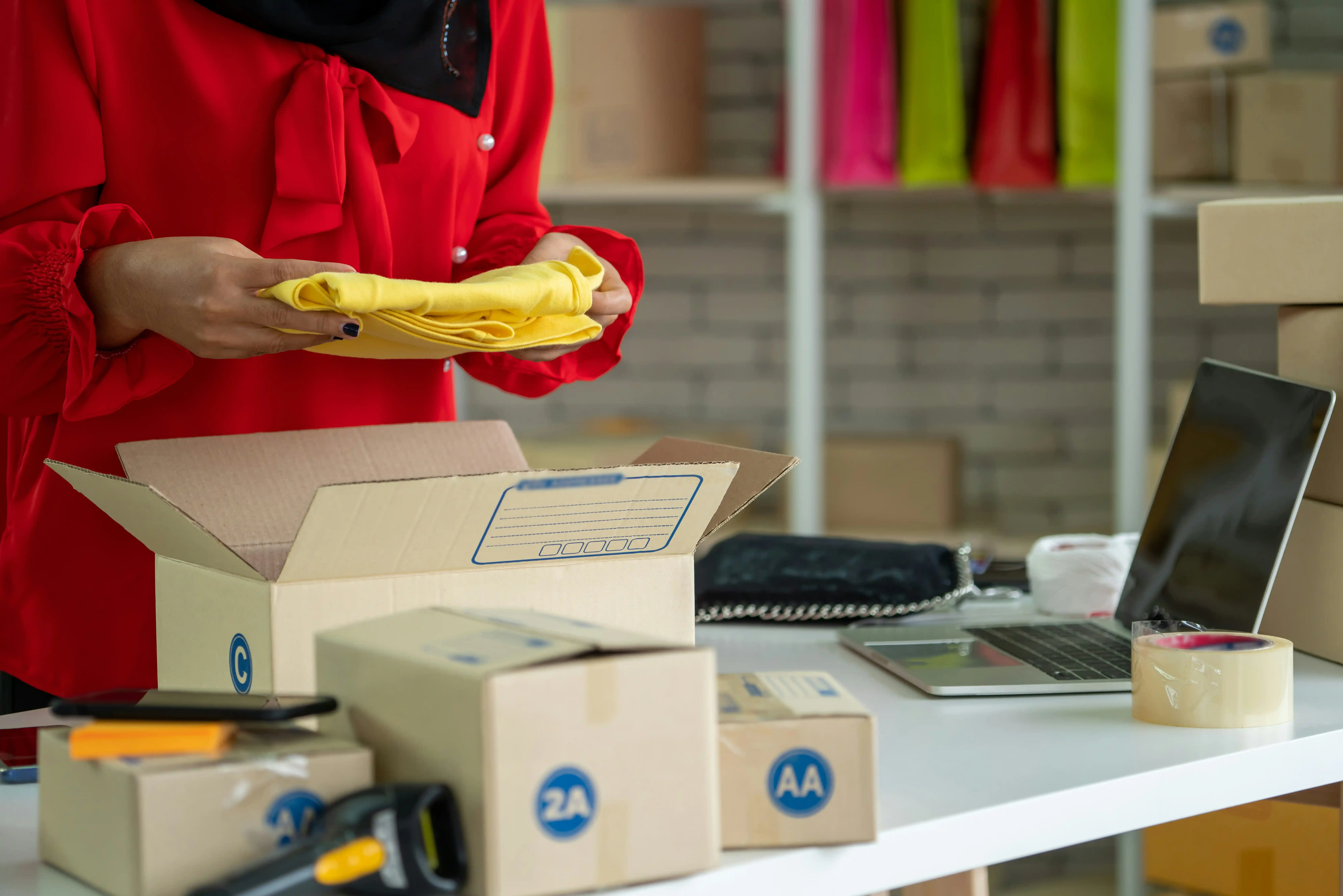 a close-up of a warehouse worker carrying out order fulfilment, packing a yellow item of clothing into a box