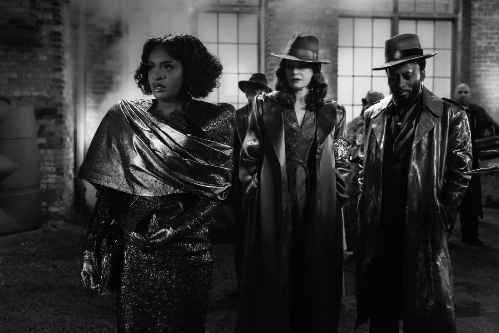 Three people wearing vintage attire, including coats and hats, stand with a serious demeanour in a noir-style black-and-white setting, evoking a classic film noir atmosphere.
