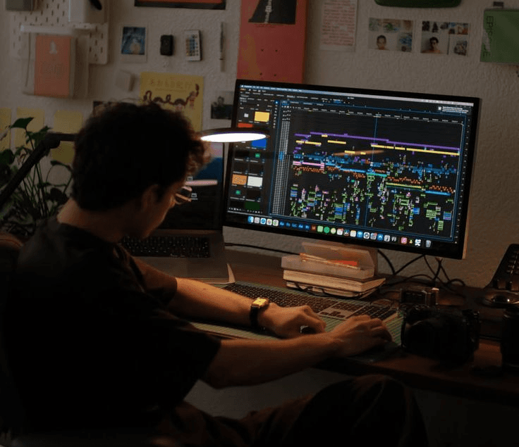 A smiling couple takes a selfie under a clear blue sky. The woman wears a red jacket, and the man, in a green top, holds a smartphone.