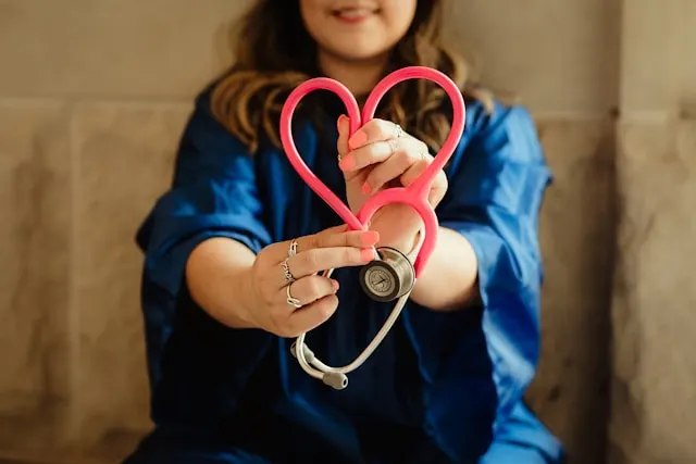 Profesional sanitaria con bata azul formando un corazón con su fonendoscopio, símbolo de la atención médica cercana del seguro de salud Allianz en Murcia