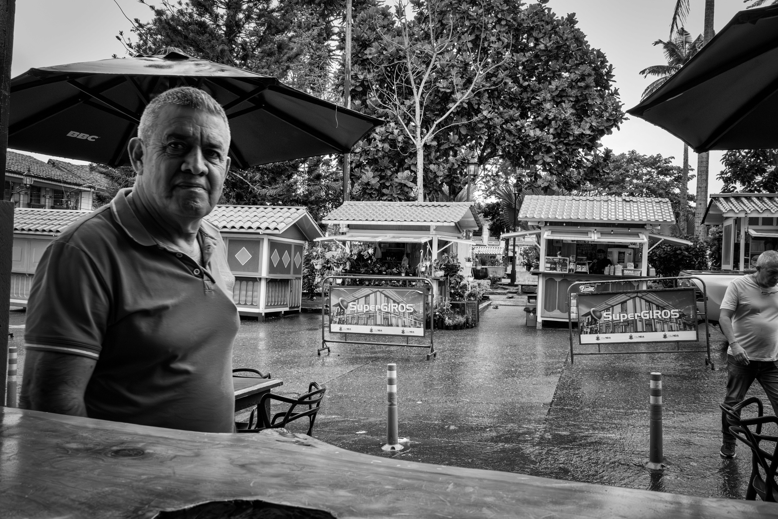 Rainy street scene with people passing by a bar window.