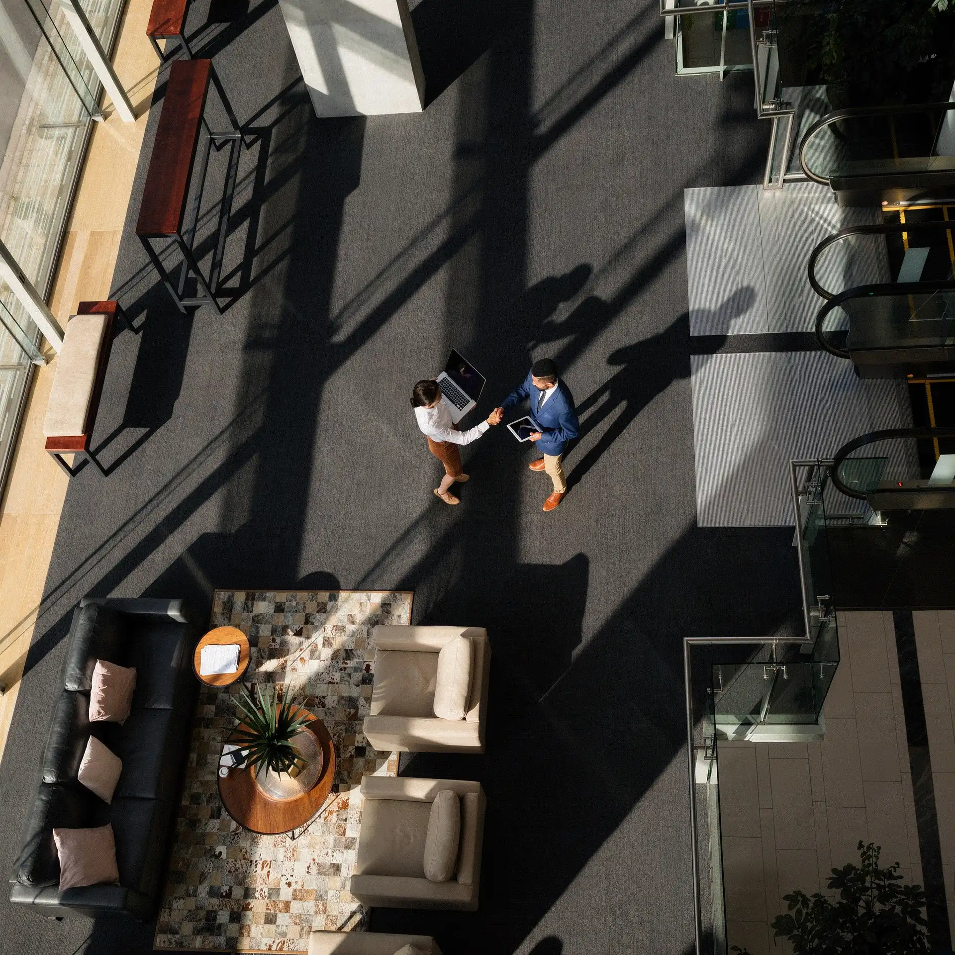 Aerial interior view of a corporate lobby, with a man and woman shaking hands over a laptop.