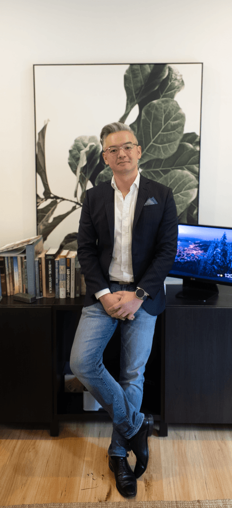 Douglas Voon leaning casually against a low console in his office, smiling.
