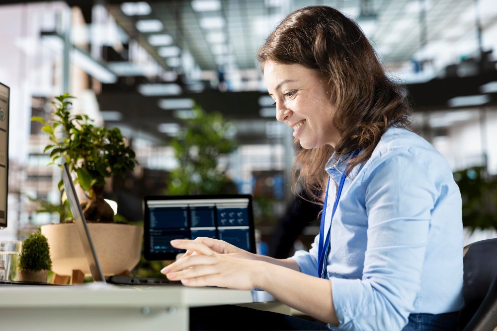 Woman smiling while using a tablet in an office, representing live workflows for tracking and logging operational tasks.