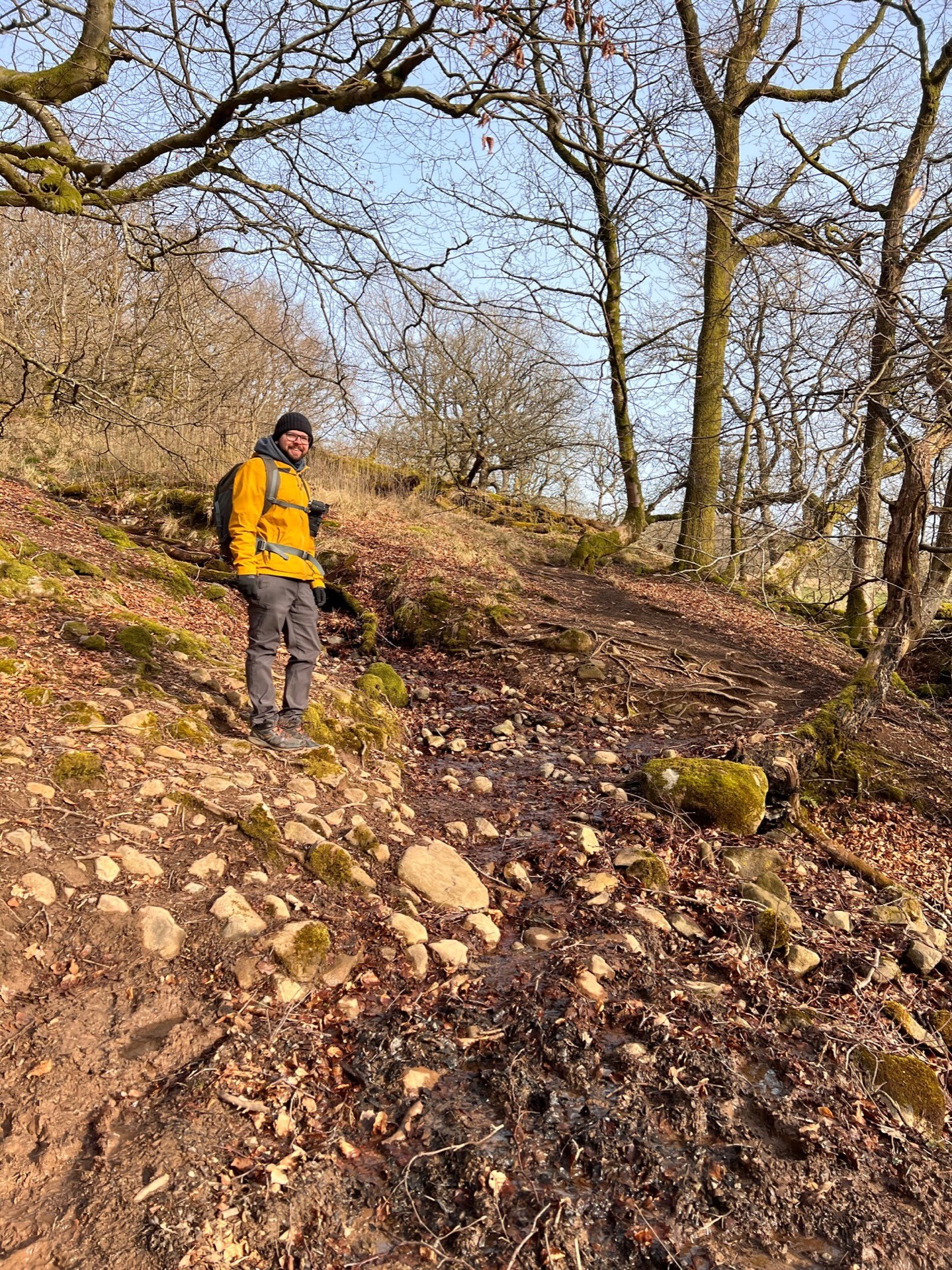 Martin is stood on the side of a muddy, stony hill, smiling.