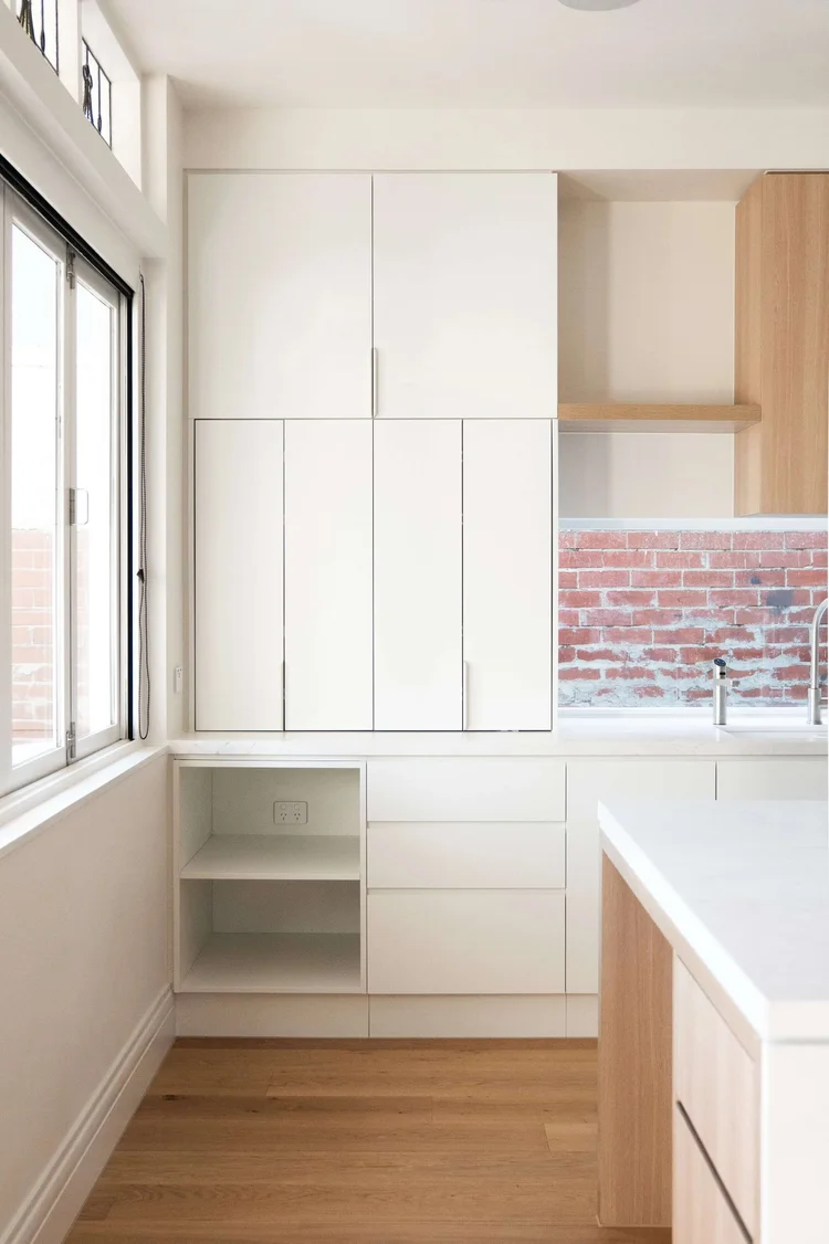 Modern kitchen with white cabinetry, wooden floors, and large windows.