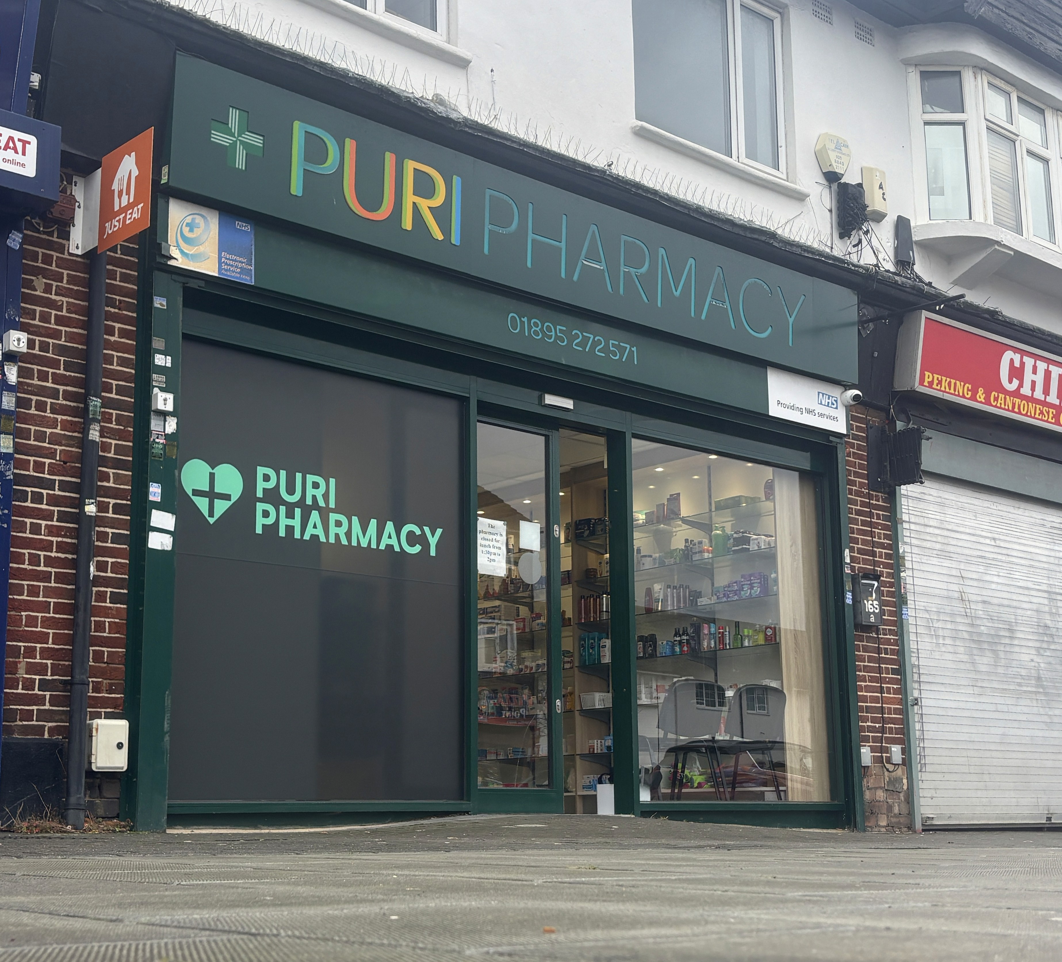 Exterior of Puri Pharmacy in West London, showing the green storefront signage with NHS services notice above the entrance.