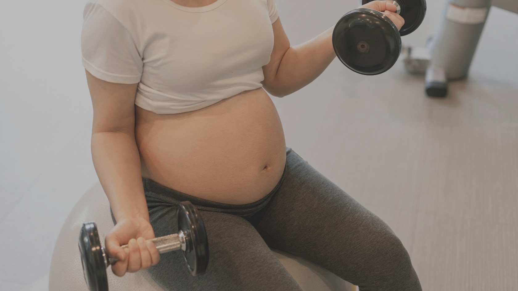 Une femme enceinte au dernier trimestre de grossesse entrain de faire du sport avec des haltères sur un ballon