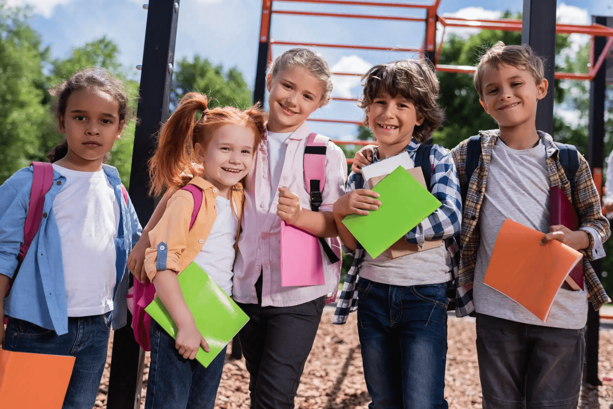 Children in the playground with rucksacks and colourful notebooks in their hands
