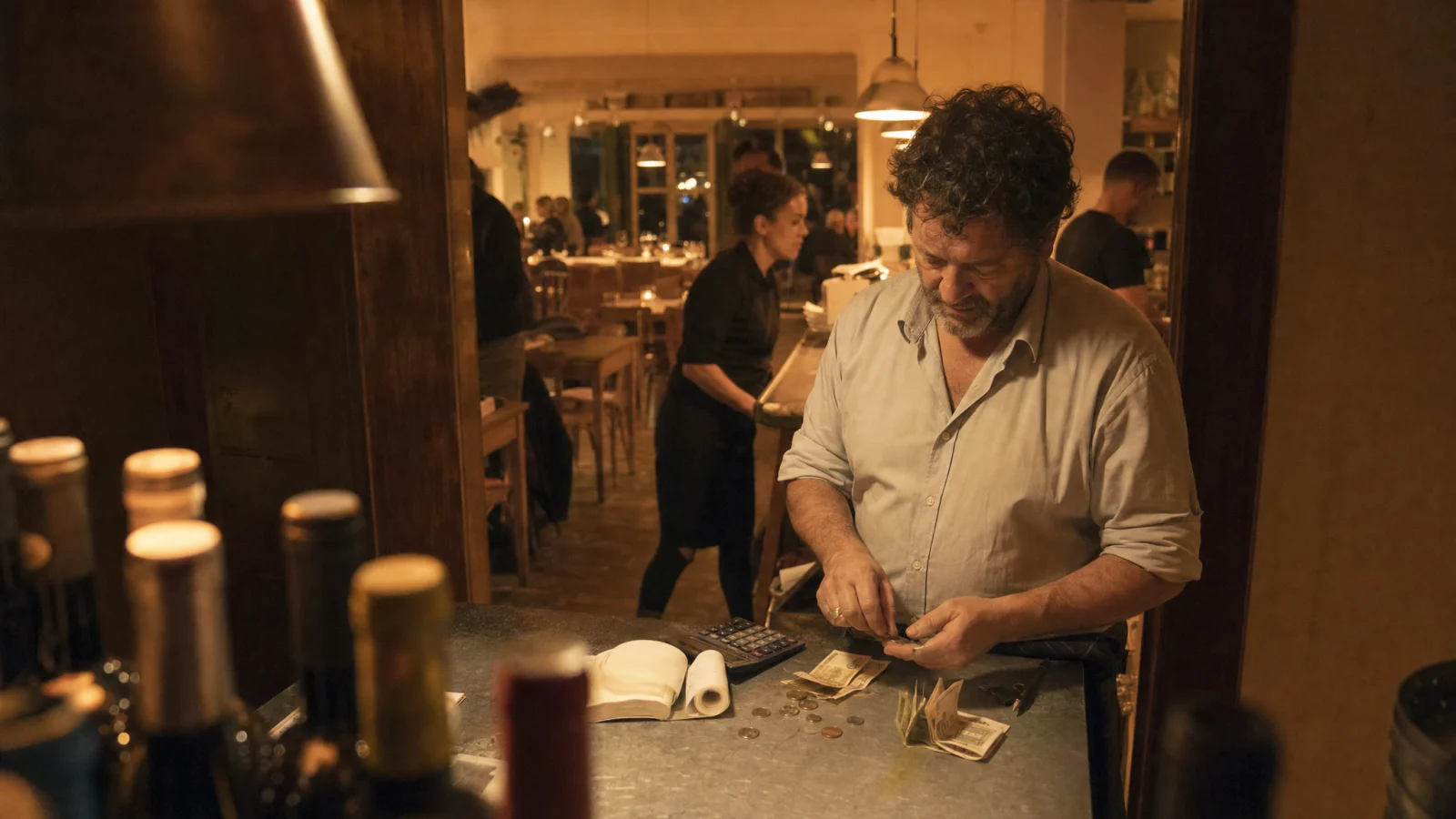 Titolare conta l'incasso della serata sul bancone del wine bar accanto a calcolatrice e quaderno