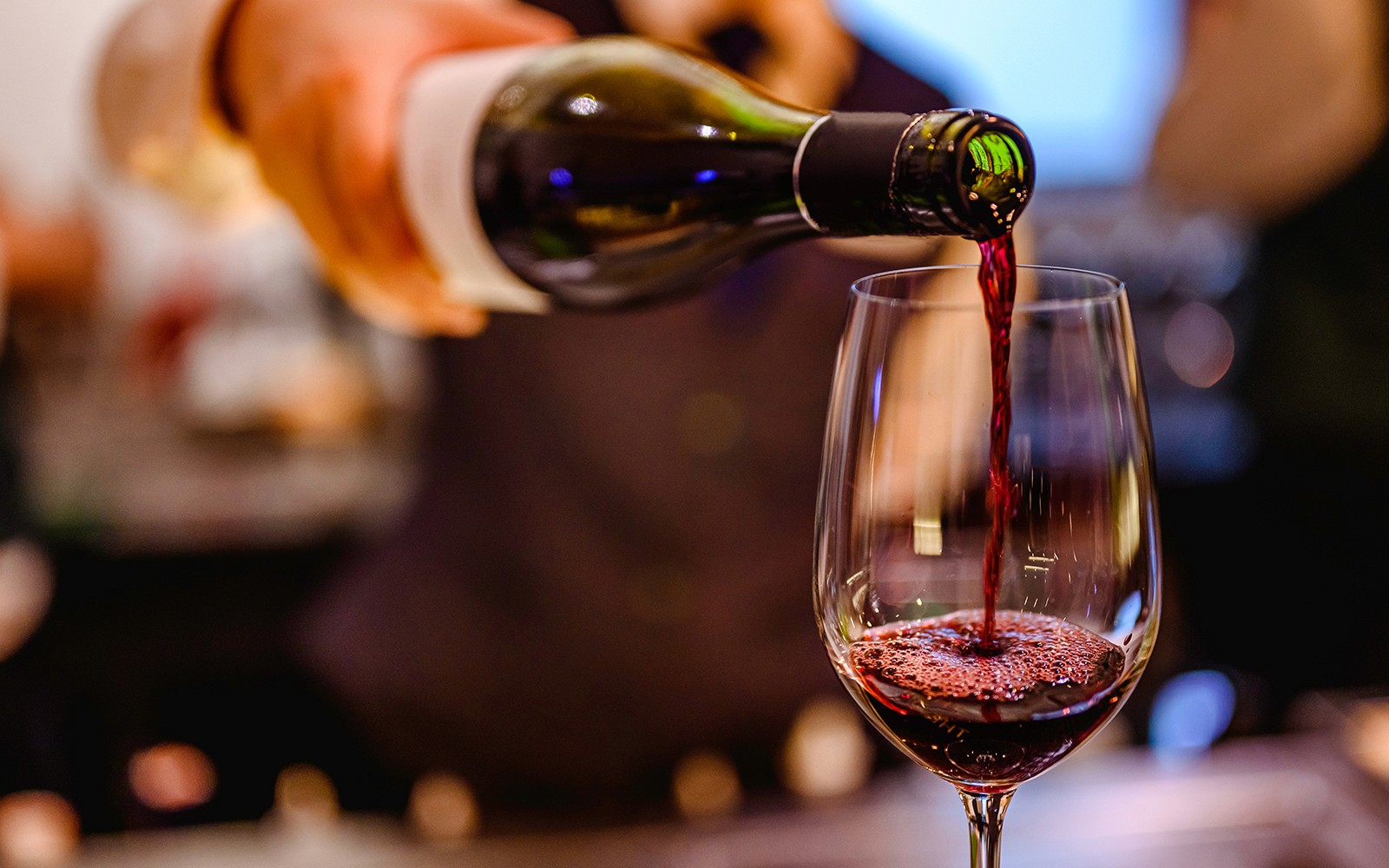 वाइन चखने के एक कार्यक्रम में एक गिलास में रेड वाइन डालना।