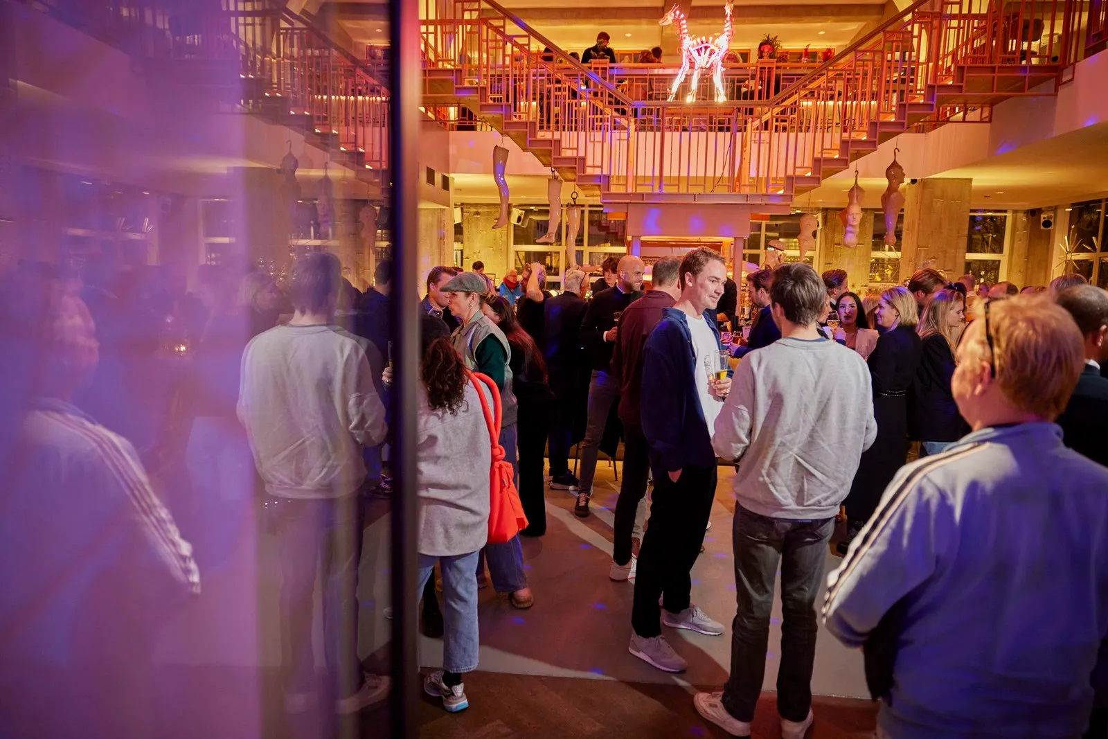 A crowd of people walking under colorful lighting, with some dressed casually and a child among them.