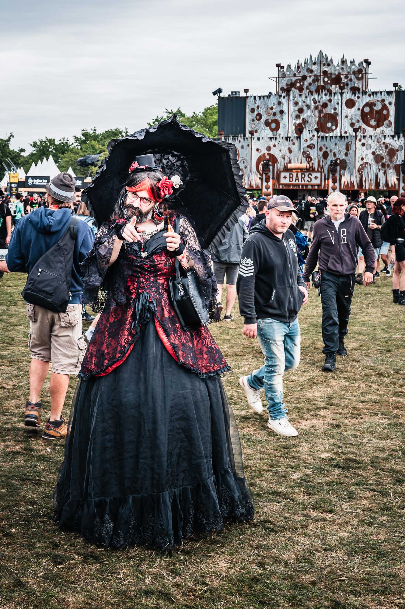 Festivalière en robe gothique rouge et noire avec ombrelle, déambulant dans le festival
