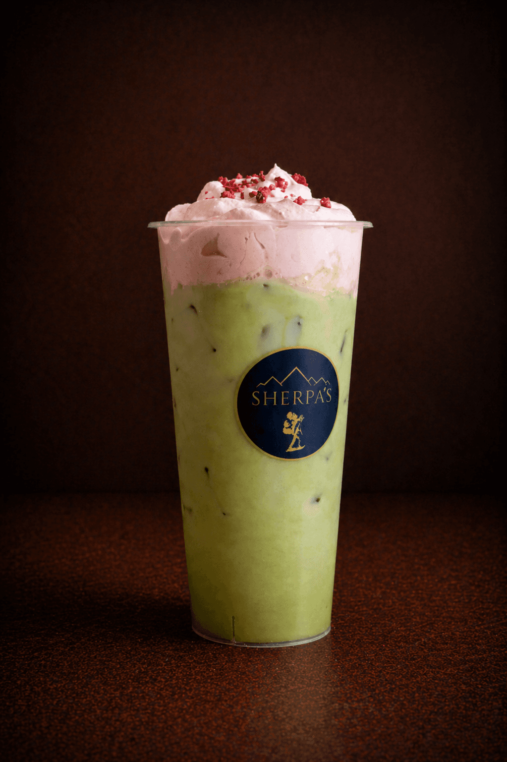 Strawberry Matcha Latte in a tall Café Sherpa's cup at Brookfield WI café. Whisked matcha over iced milk finished with strawberry sweet cream and dried strawberries.