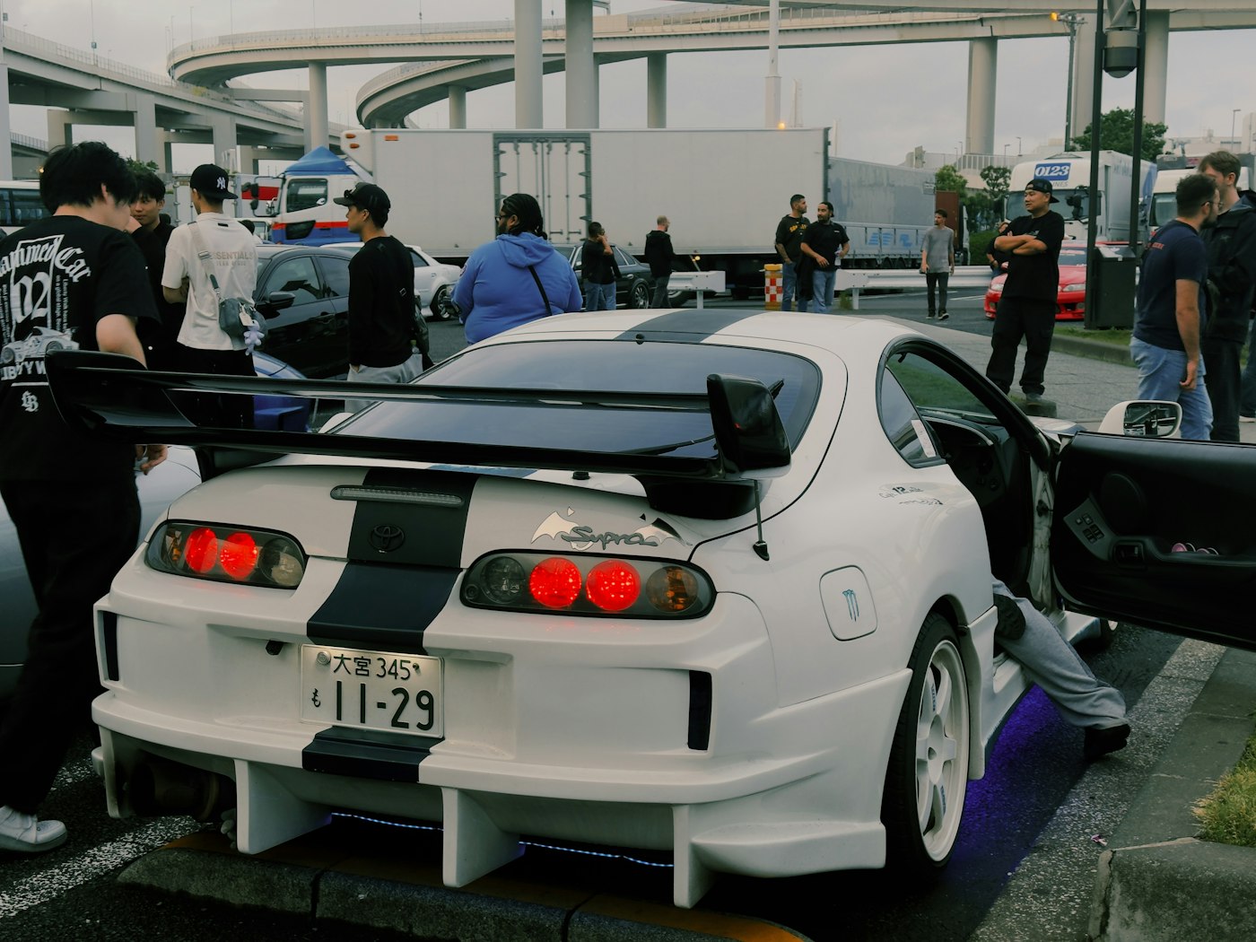 Modified Toyota Supra with a crowd gathered, car-meet culture - stand-in placeholder, not final