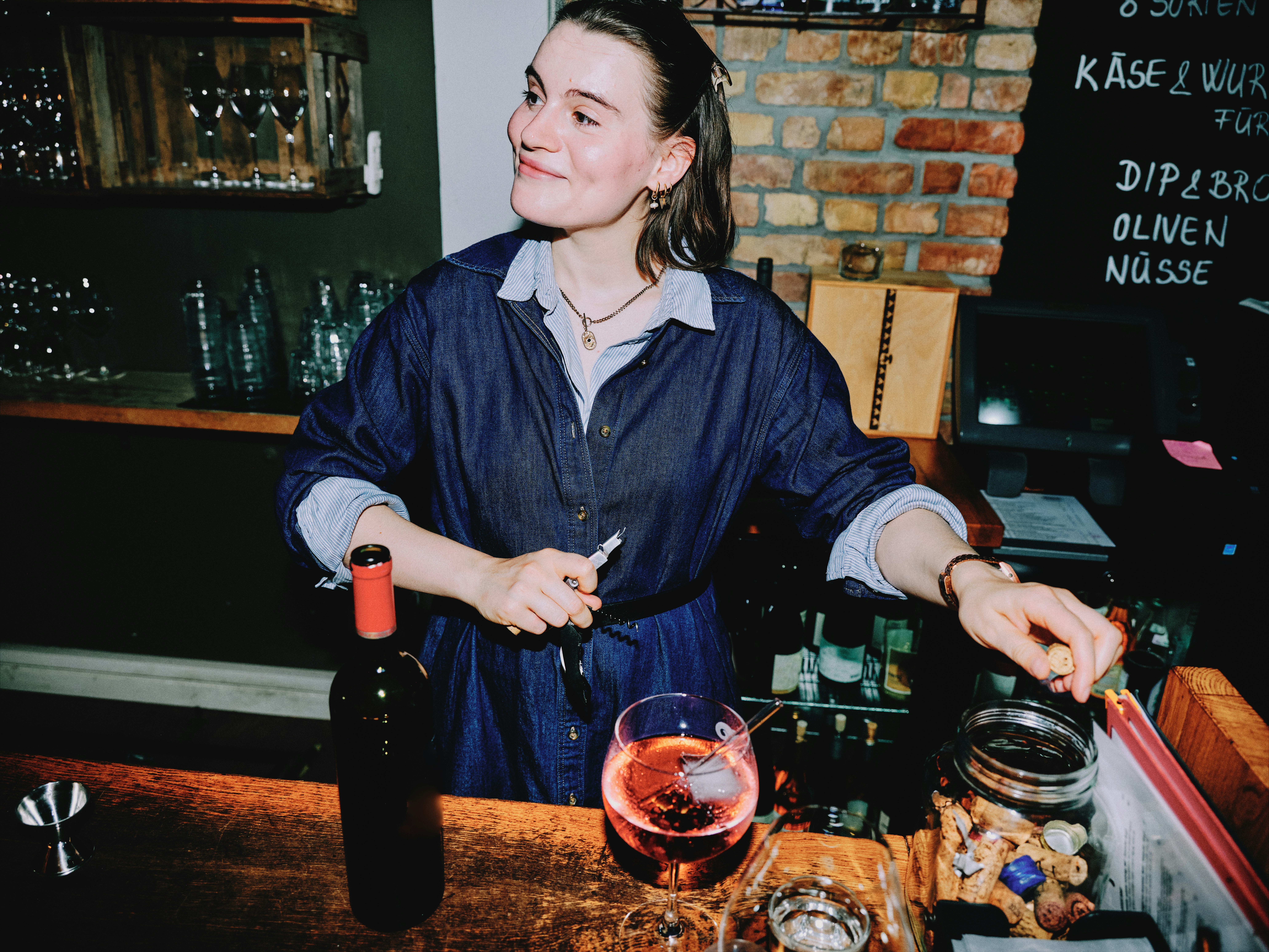female bartender pouring wine overhead at a rustic wine bar with wooden crate shelving