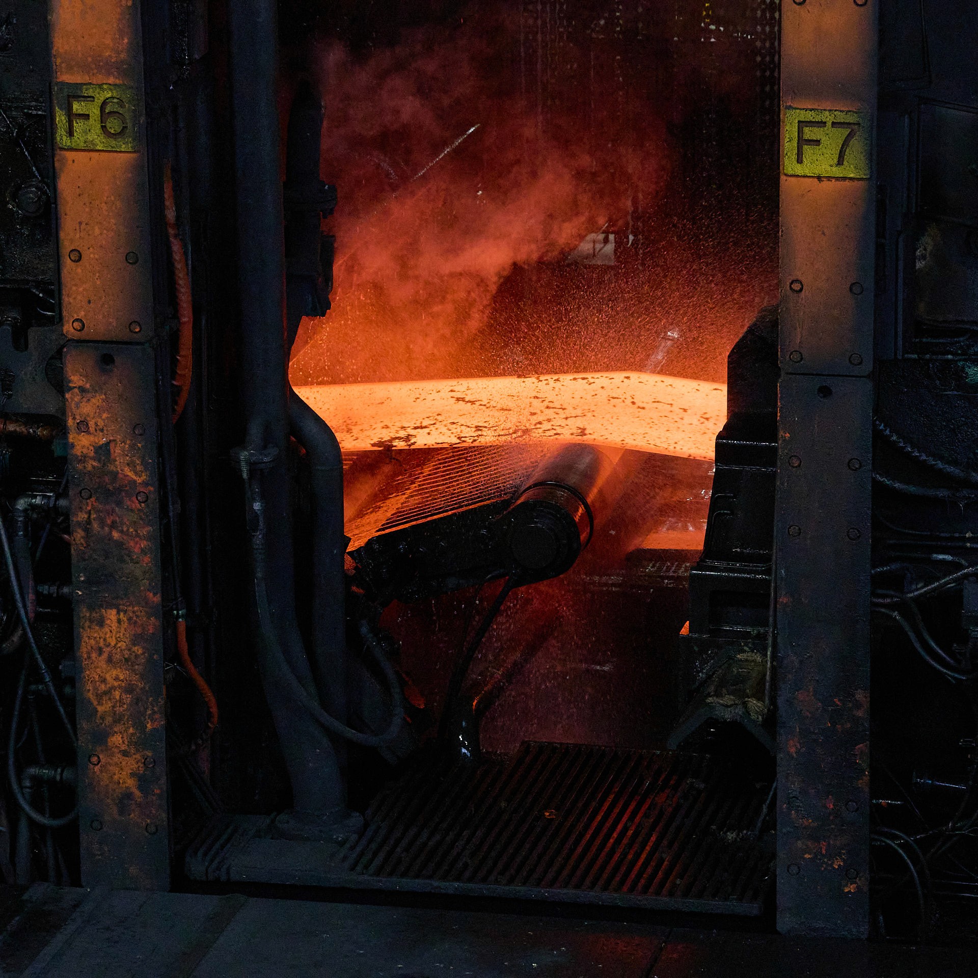 Gros plan sur une plaque d'acier en fusion rouge vif sortant d'un laminoir industriel, générant de la vapeur d'eau.
