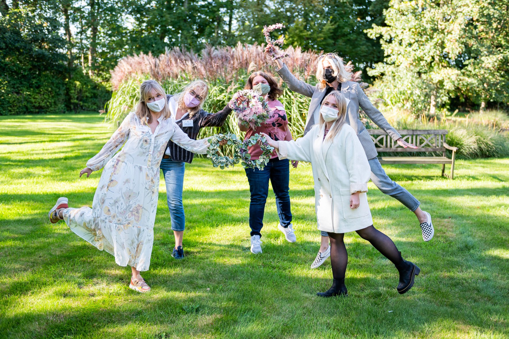 Die Creator zeigen im Kreis stehend auf einer grünen Wiese ihre Blumenkränze aus dem Workshop mit Hygge.