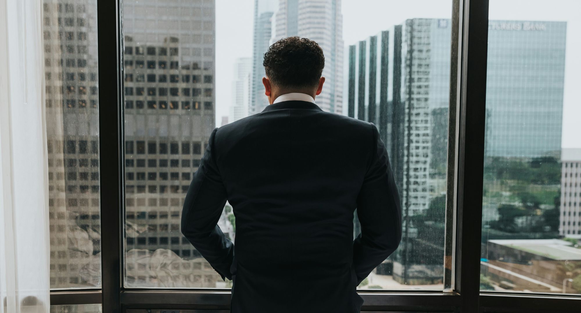 homem colocando as mãos no bolso enquanto está em frente à parede de vidro