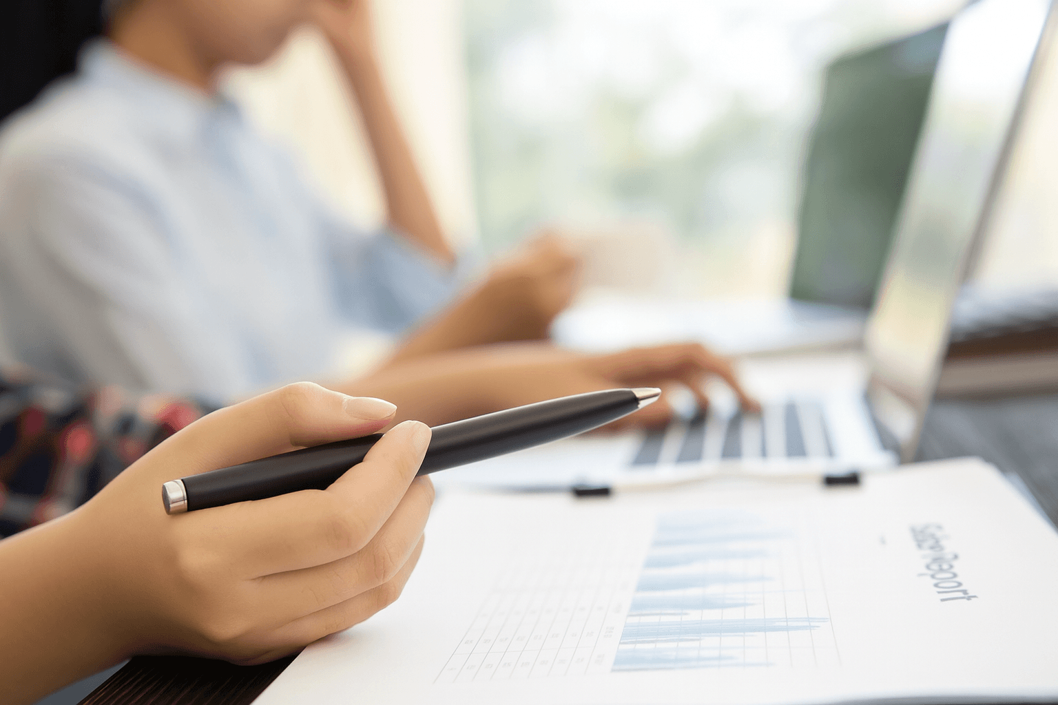 Une personne tenant un stylo et consultant des documents financiers, avec un ordinateur en arrière-plan, symbolisant la création et la gestion d’un compte vendeur sur Amazon.