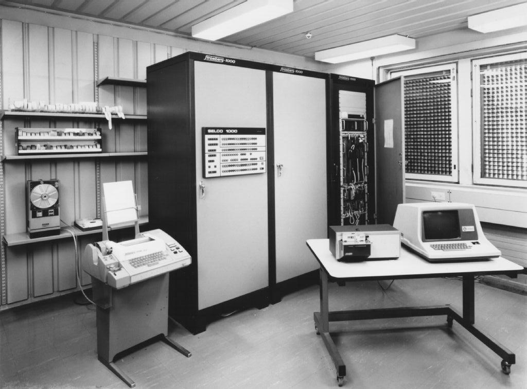 Black-and-white photo of a retro office with some computer and fax equipment.