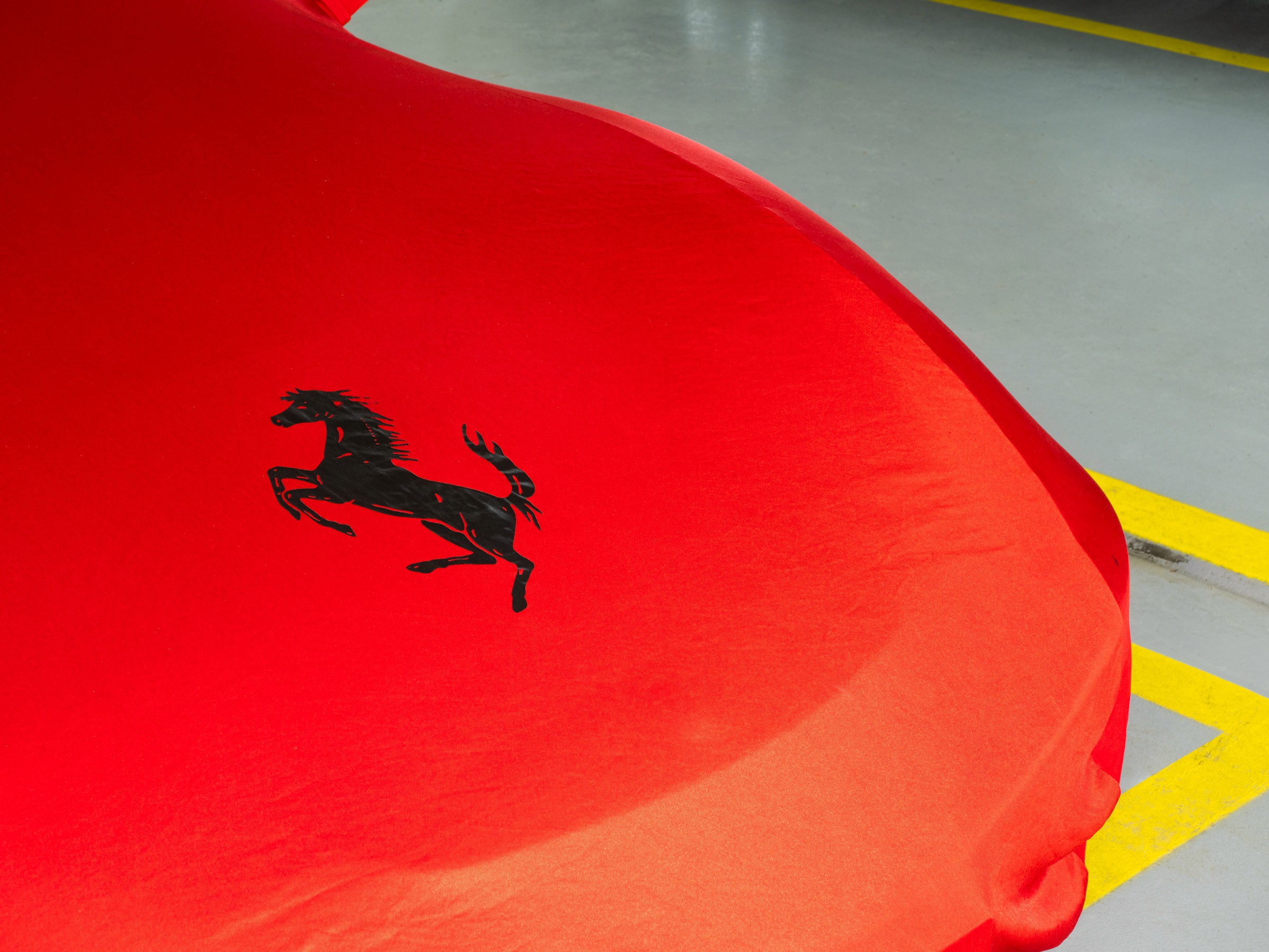 Gros plan sur le capot d'une Ferrari recouvert par une couverture rouge de la marque et d'un gros logo Ferrari