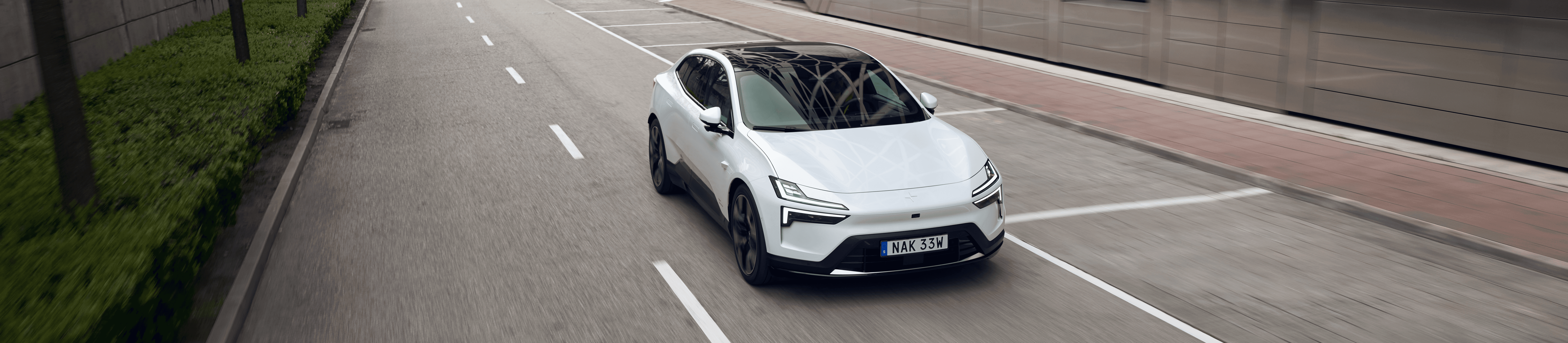 Polestar 4 blanche en conduite urbaine avec vue avant dans un environnement architectural moderne