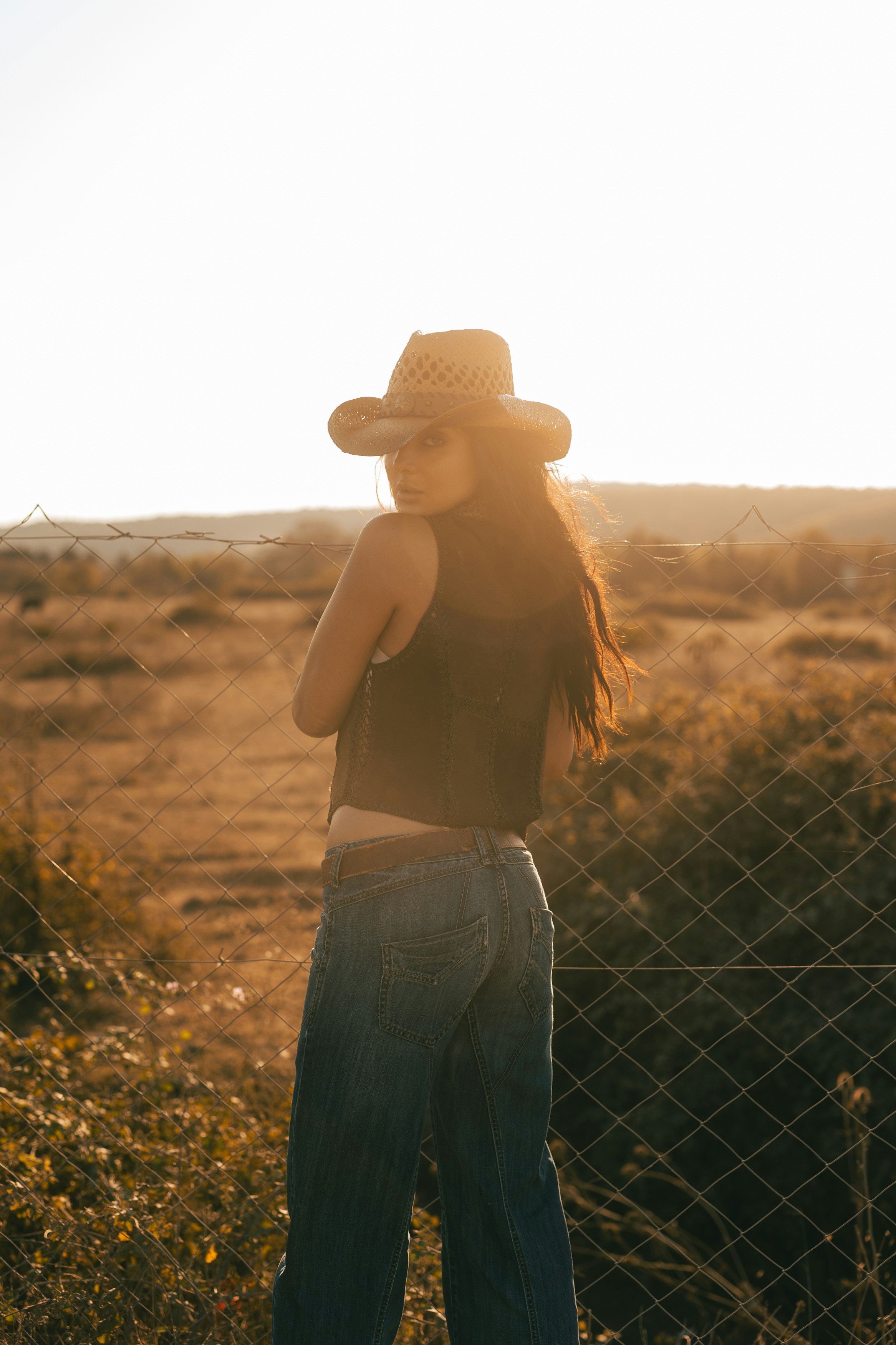 Woman in cowboy hat looking over shoulder at sunset