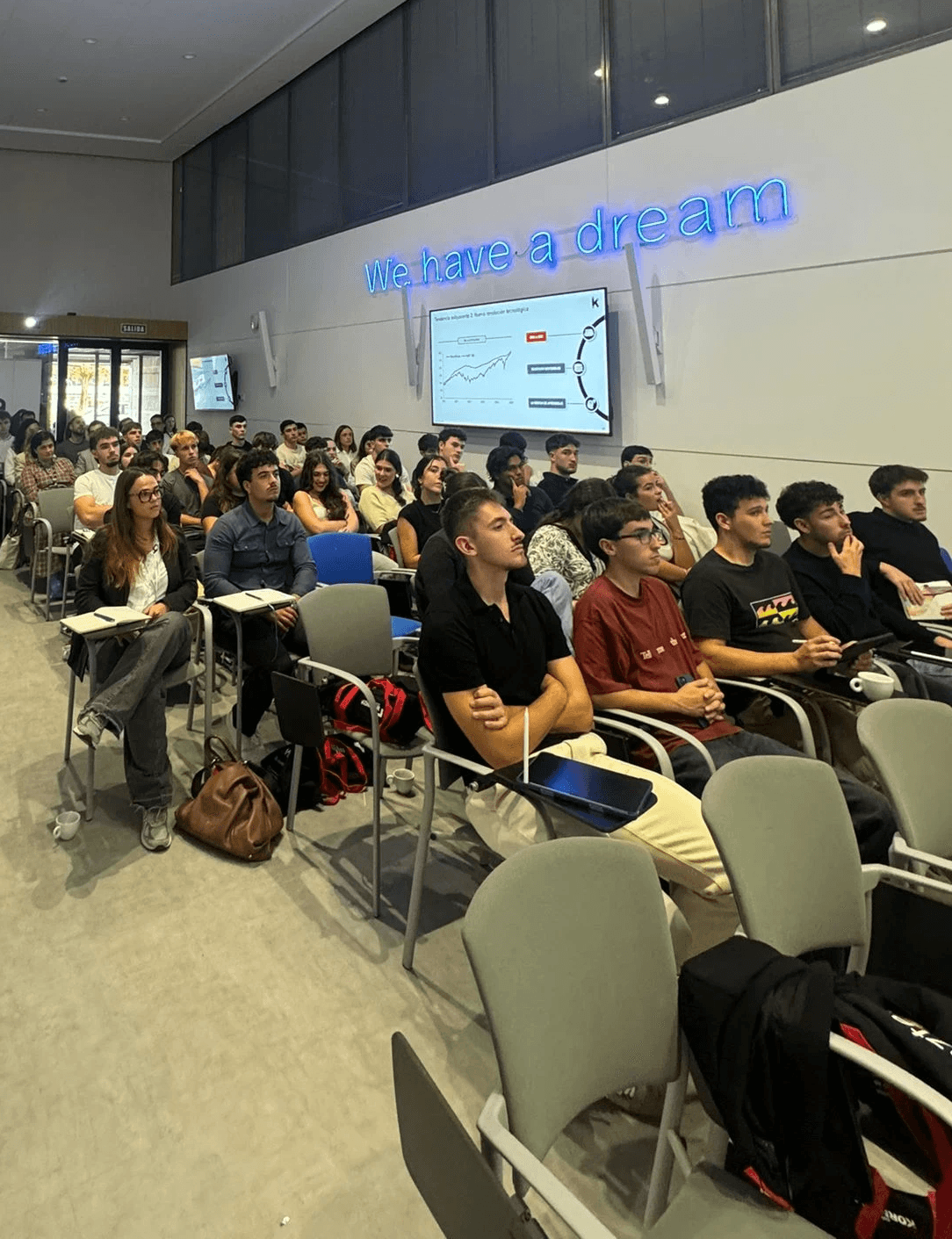 A smiling young man with crossed arms, wearing a plaid shirt and white t-shirt, poses against a dark background.