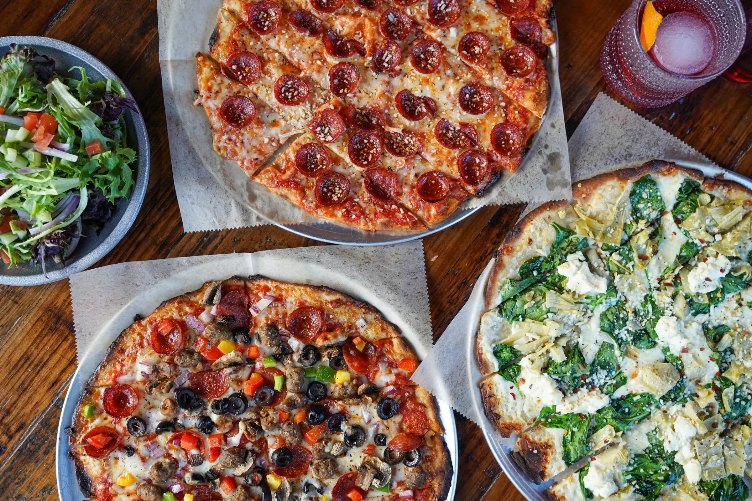Pizzas and a salad on a wood table
