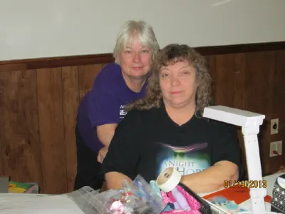 Two women chatting at a crop table beside a craft lamp