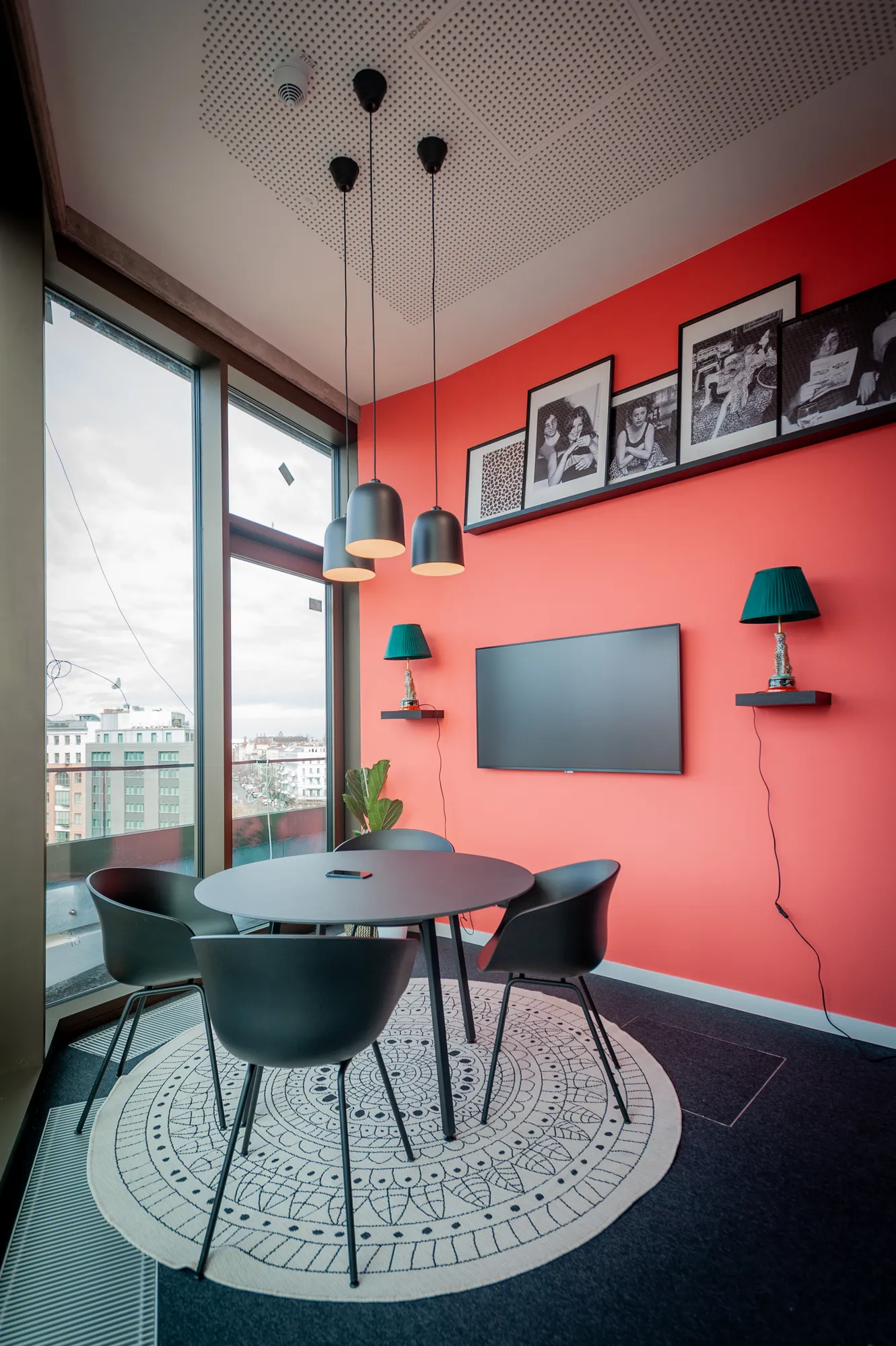 Meeting niche with coral wall, round black table, chairs and framed black-and-white photos.