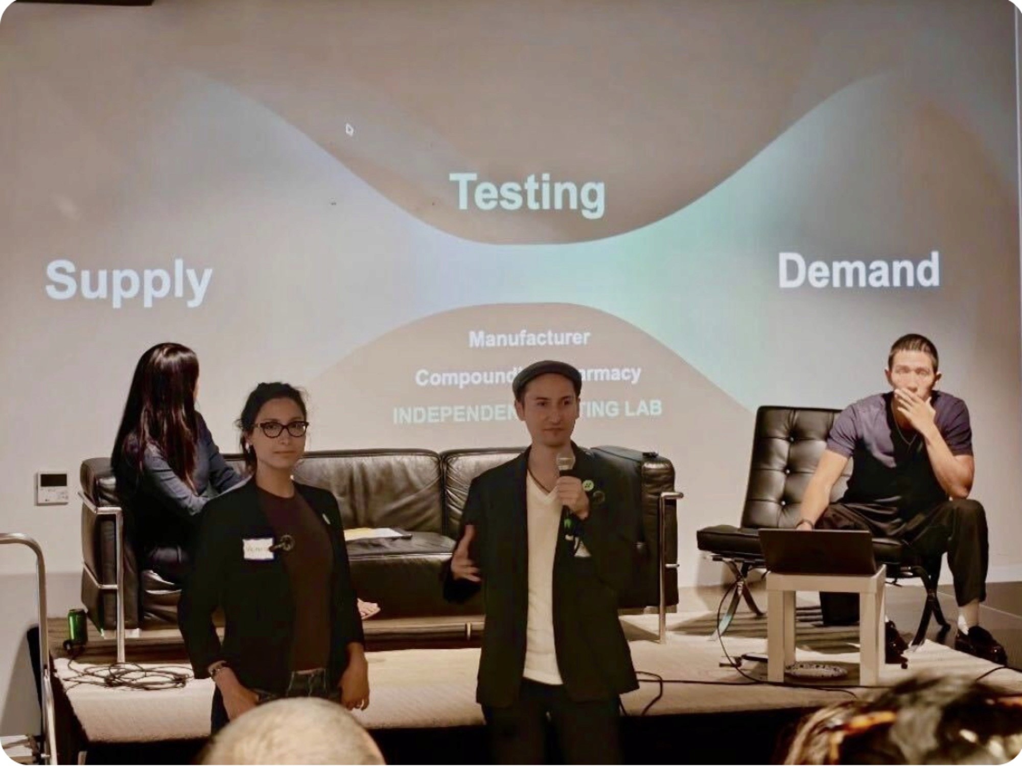 Three members of the Sapho Bio team presenting on stage at the Peptides for Women event, with a Supply-Testing-Demand slide projected behind them